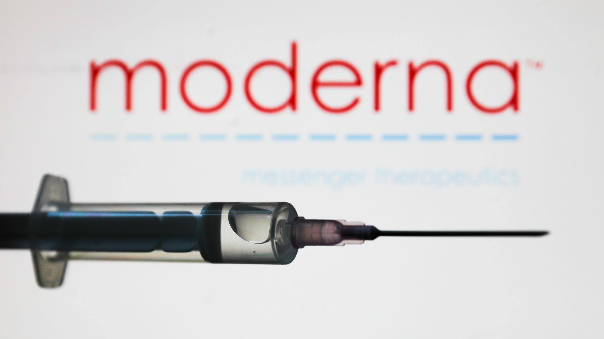 Moderna's red logo in the background with a vaccine syringe in the foreground.