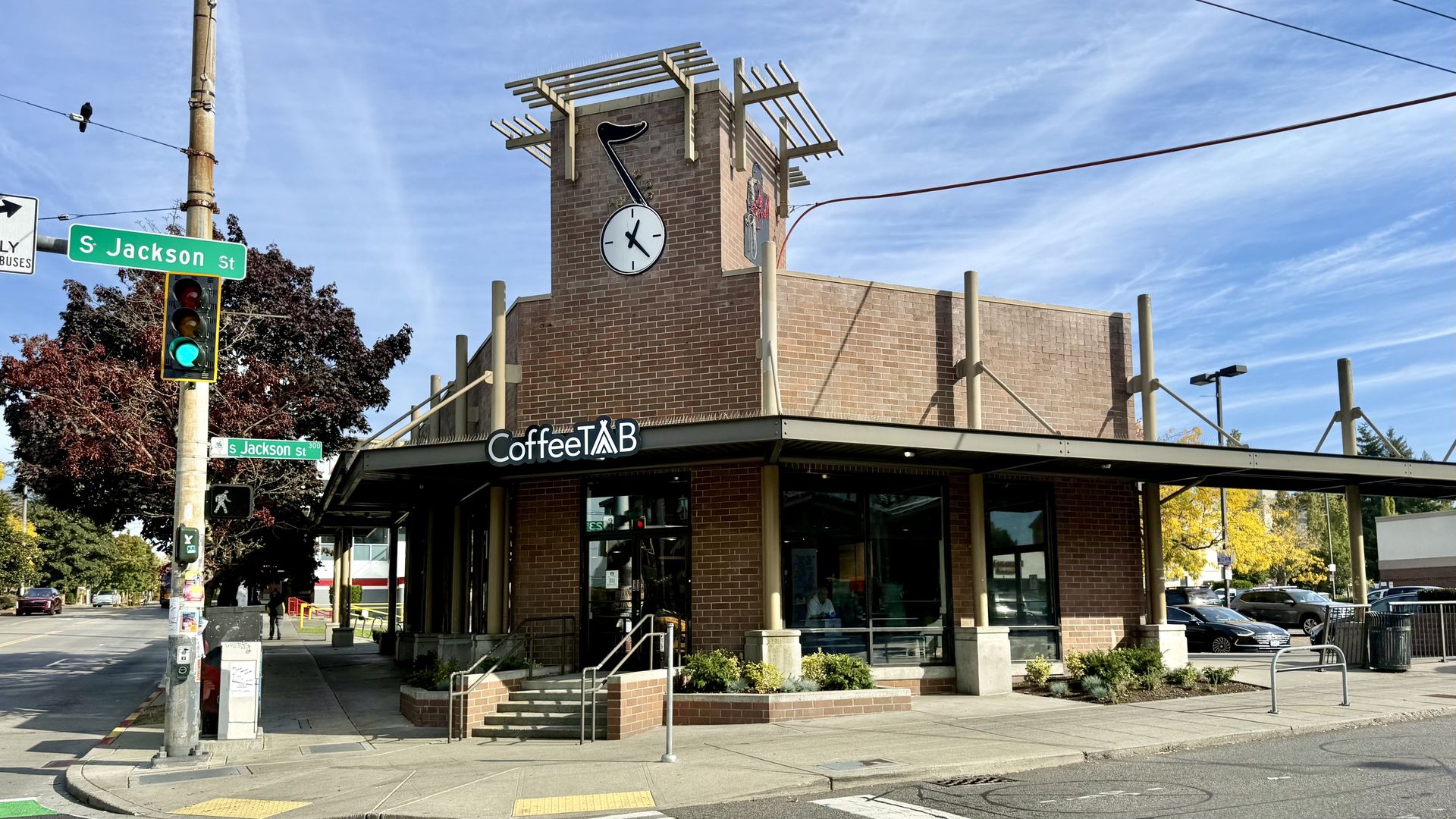 Brick clock-tower building under construction with wooden scaffolding. At the corner, green S Jackson St signs; CoffeeTAB storefront below; clear blue sky.