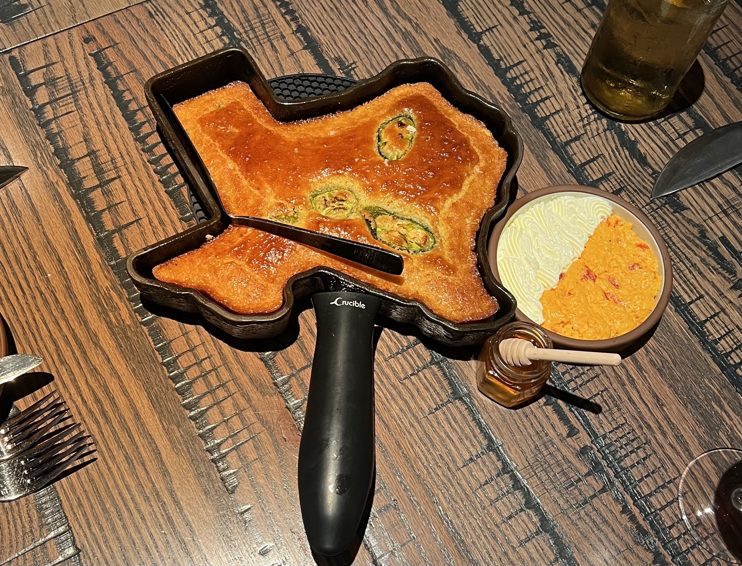 A Texas-shaped cornbread sits on a wooden table, accompanied by toppings.