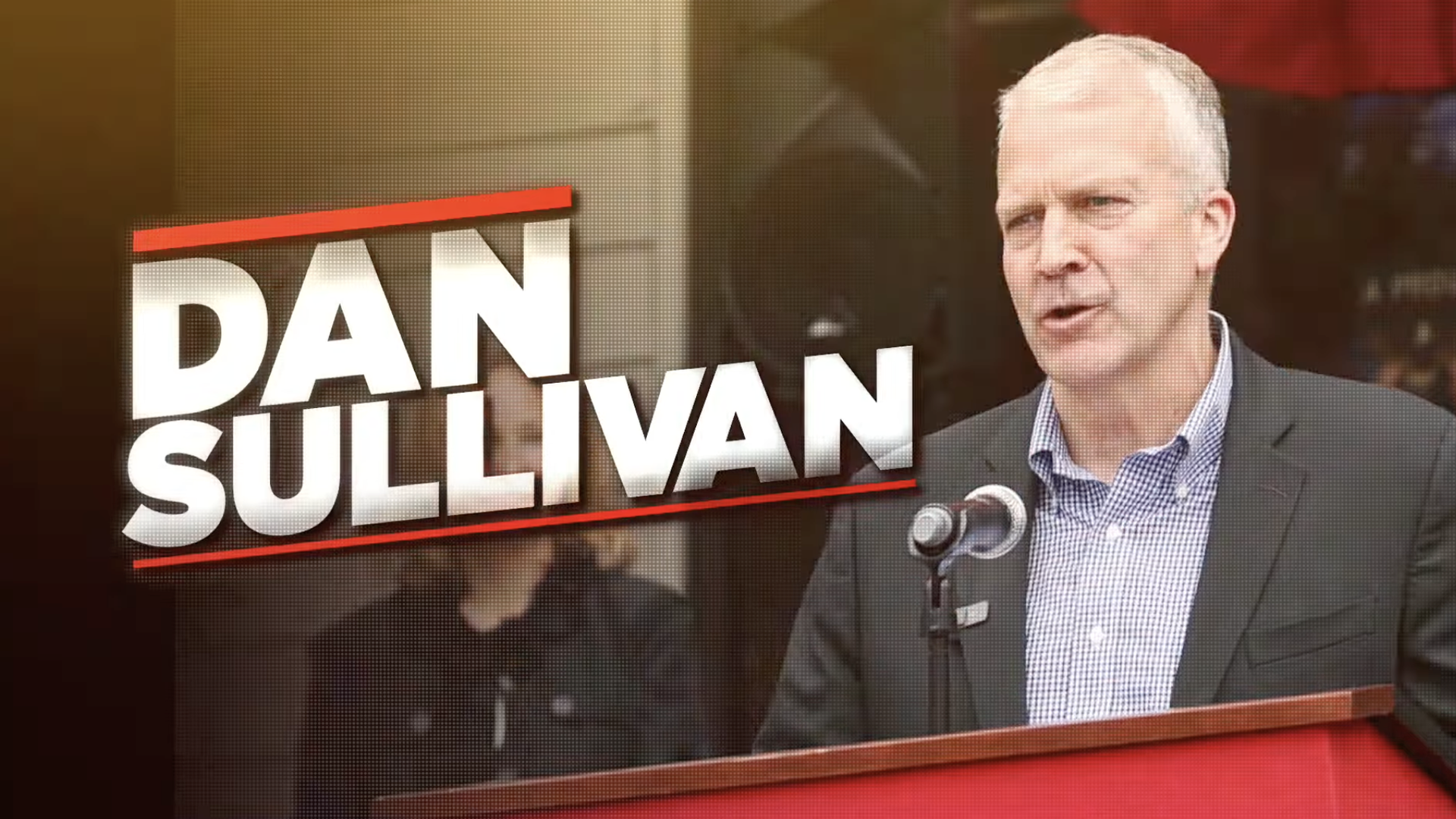 Man in a dark suit speaks at a podium with a microphone; large white text reads "DAN SULLIVAN" with red accents on the left and a warm studio backdrop.