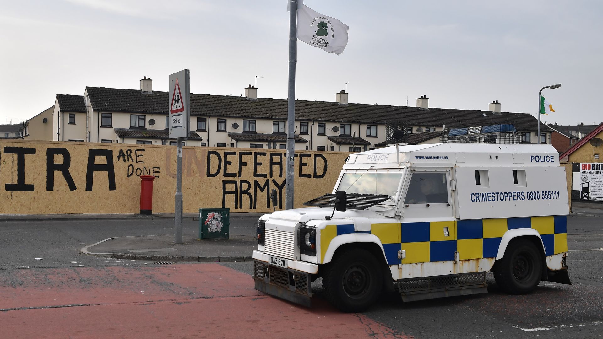 In this image, an ambulance is parked on a street with a wall behind it that reads "IRA are done: Defeated Army"