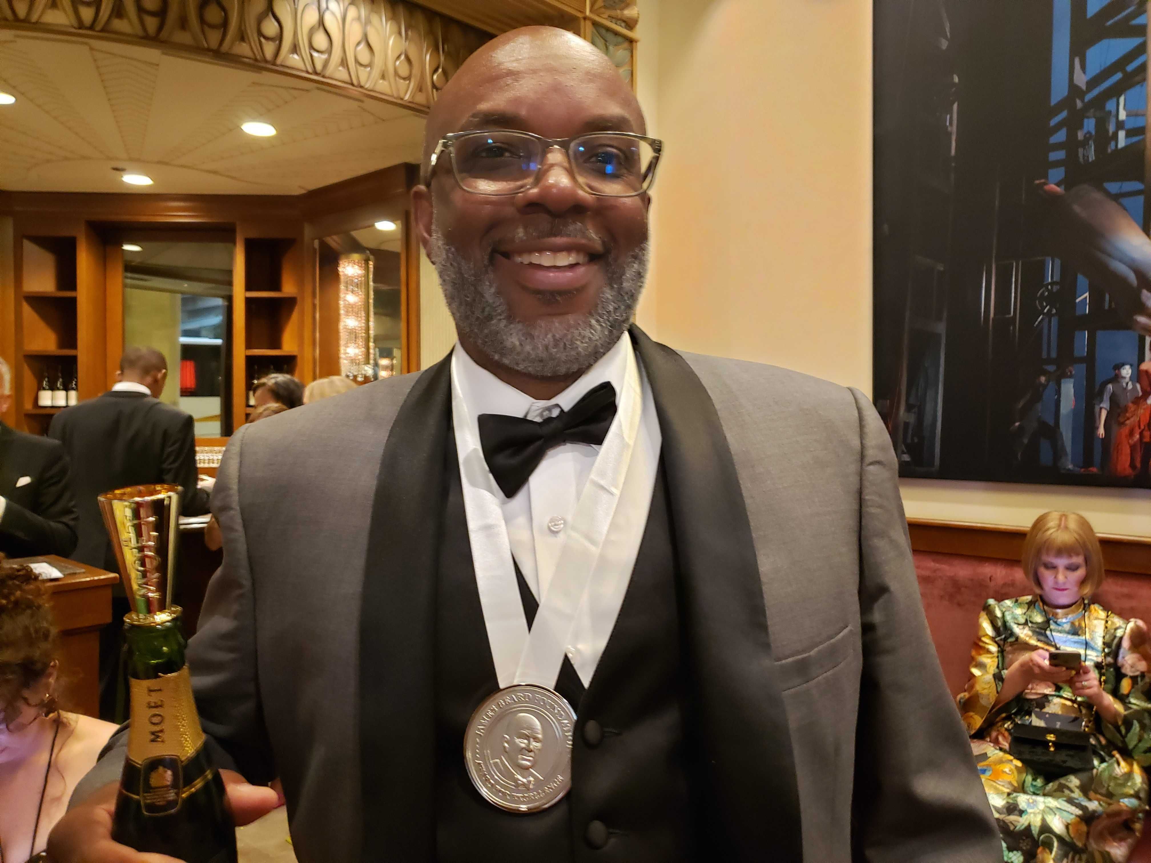 photo of Ricky Moore in a tuxedo after winning a James Beard Award, with the award around his neck