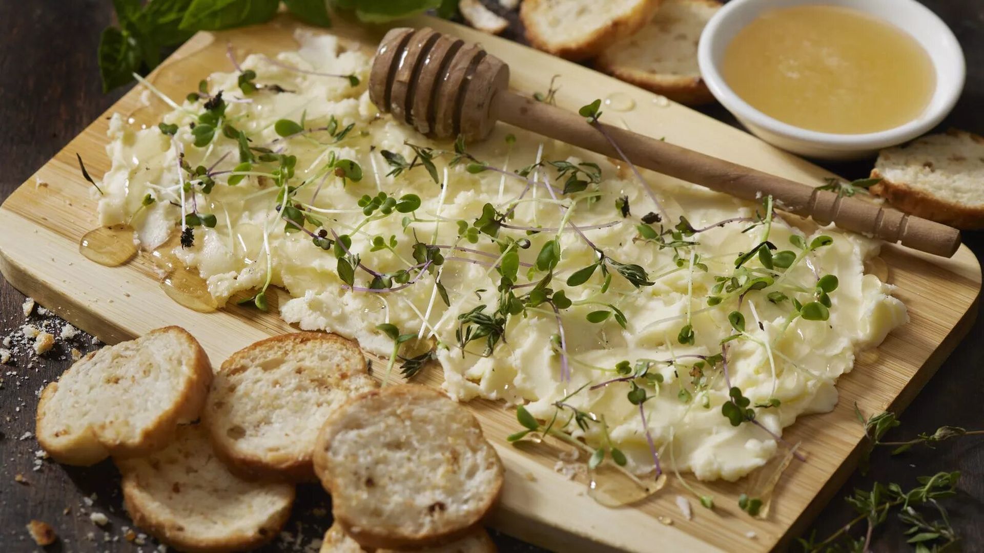 Butter is covered in honey and herbs, spread across a wooden board.