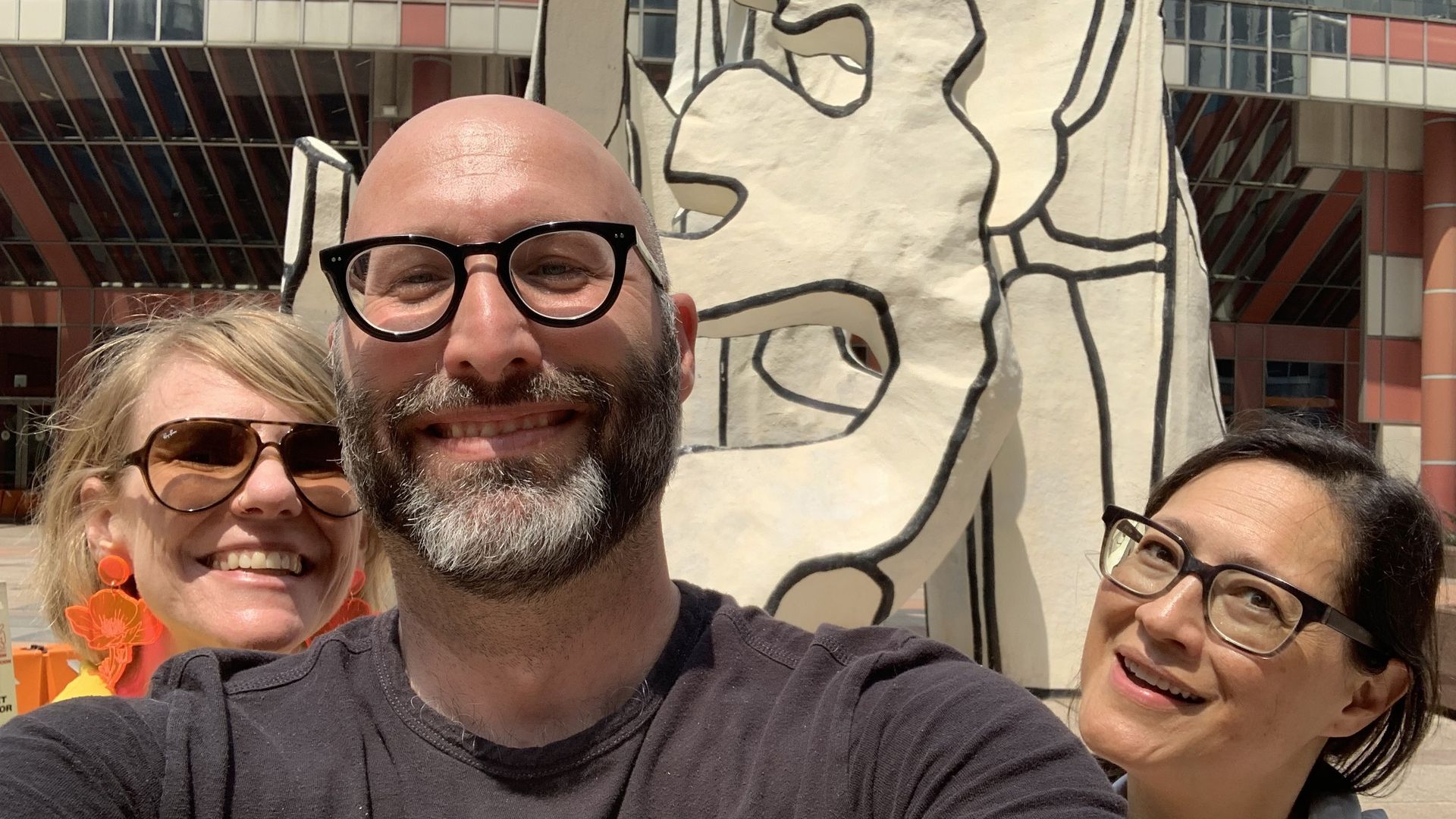 Three smiling faces in front of white and black sculpture.