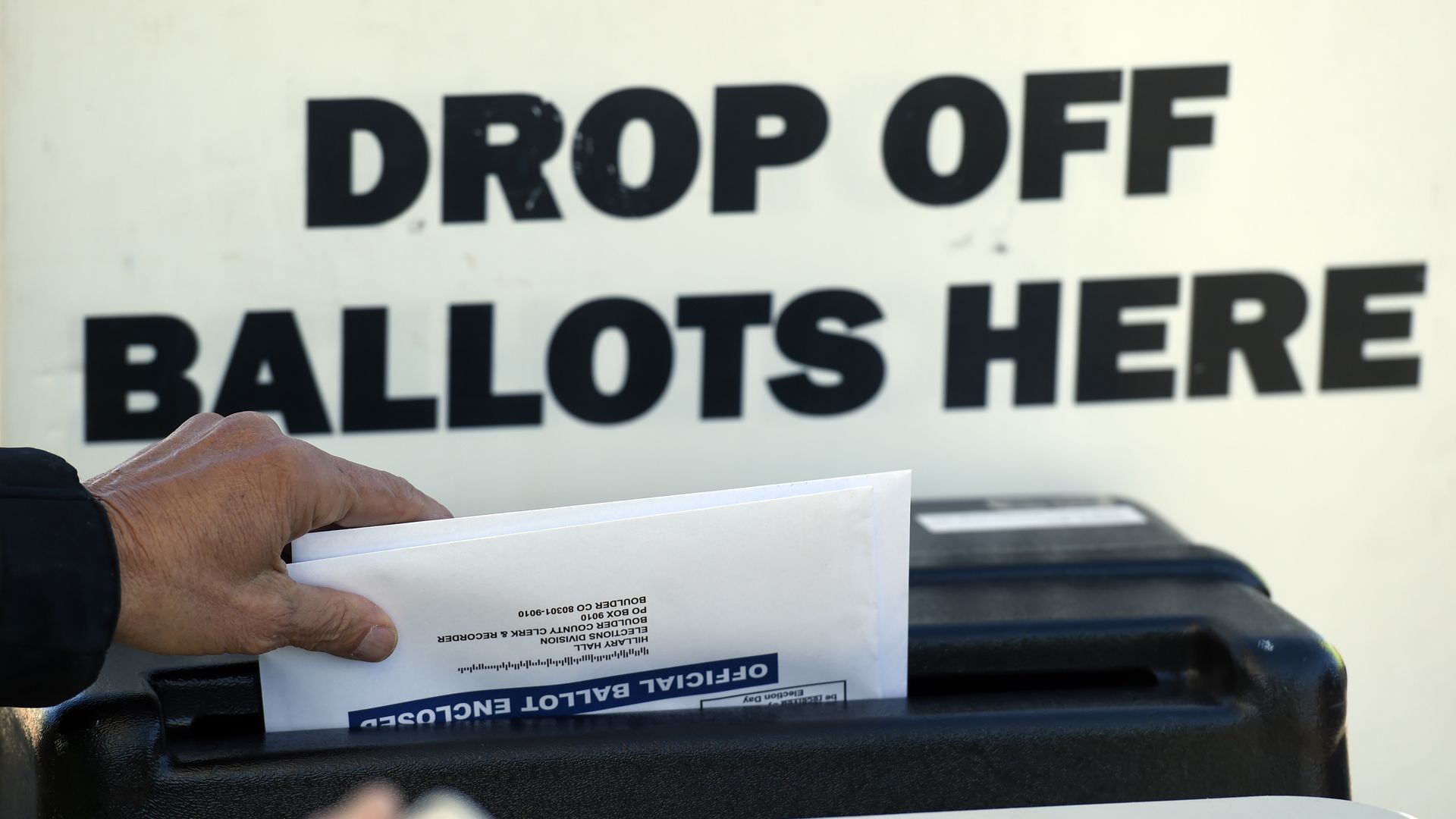 Ballots being dropped in box that under sign that says "Drop of ballots here"
