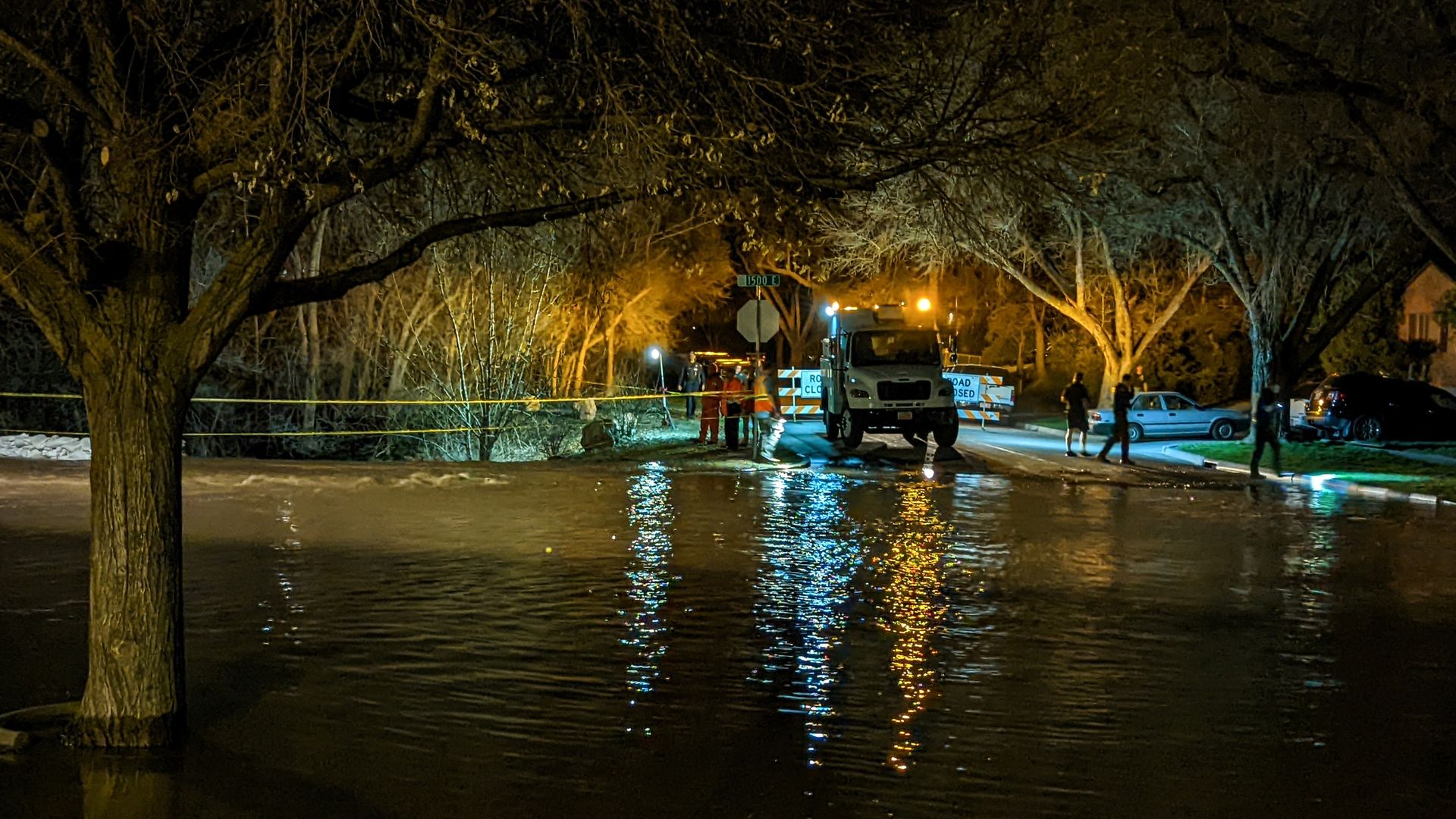 A street is flooded at night while crews and volunteers walk around the edges of the water.