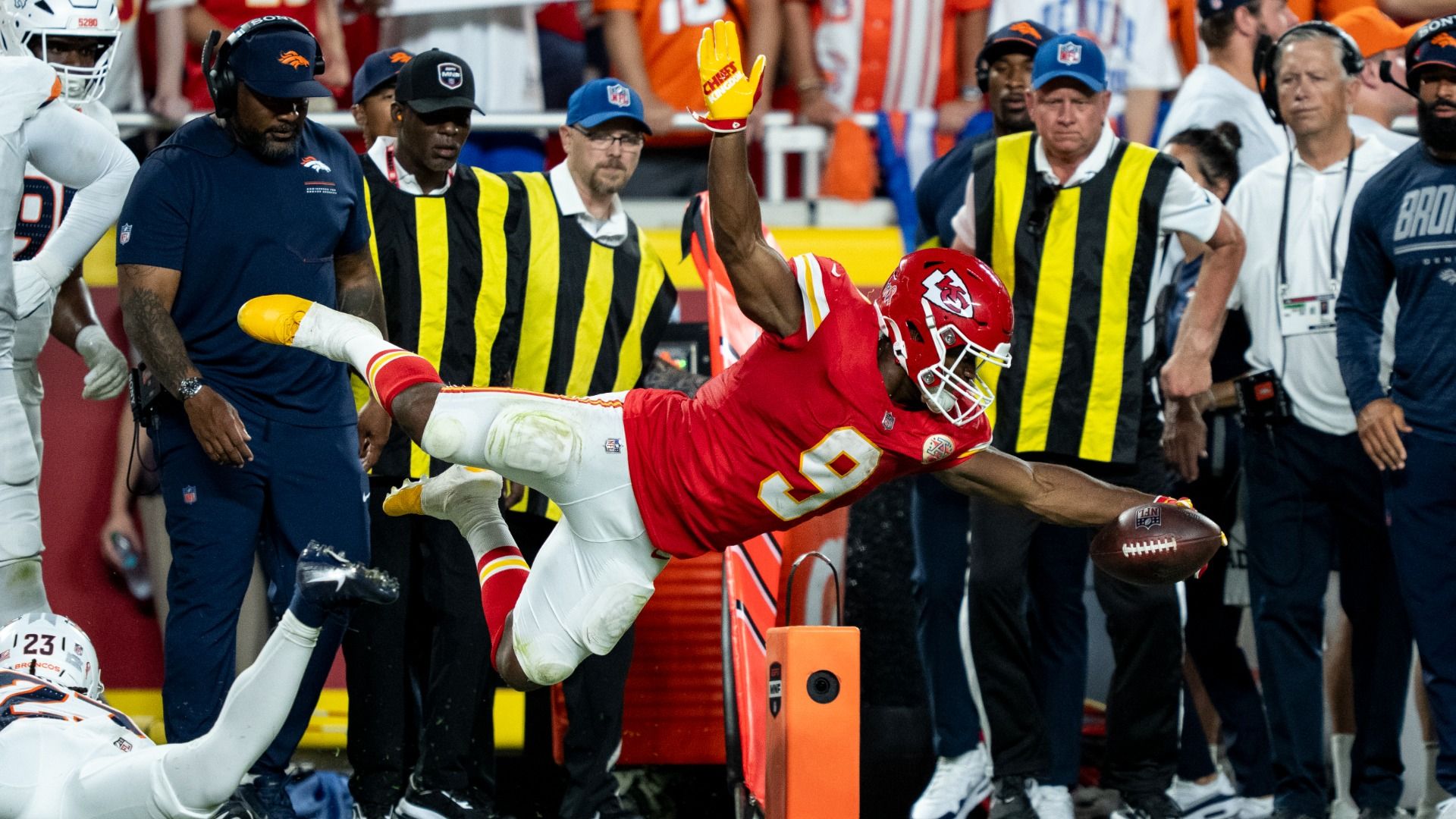 Chiefs No. 9 Kenneth Walker dives with his arms outstretched to reach the football across the orange pylon mid-air. 