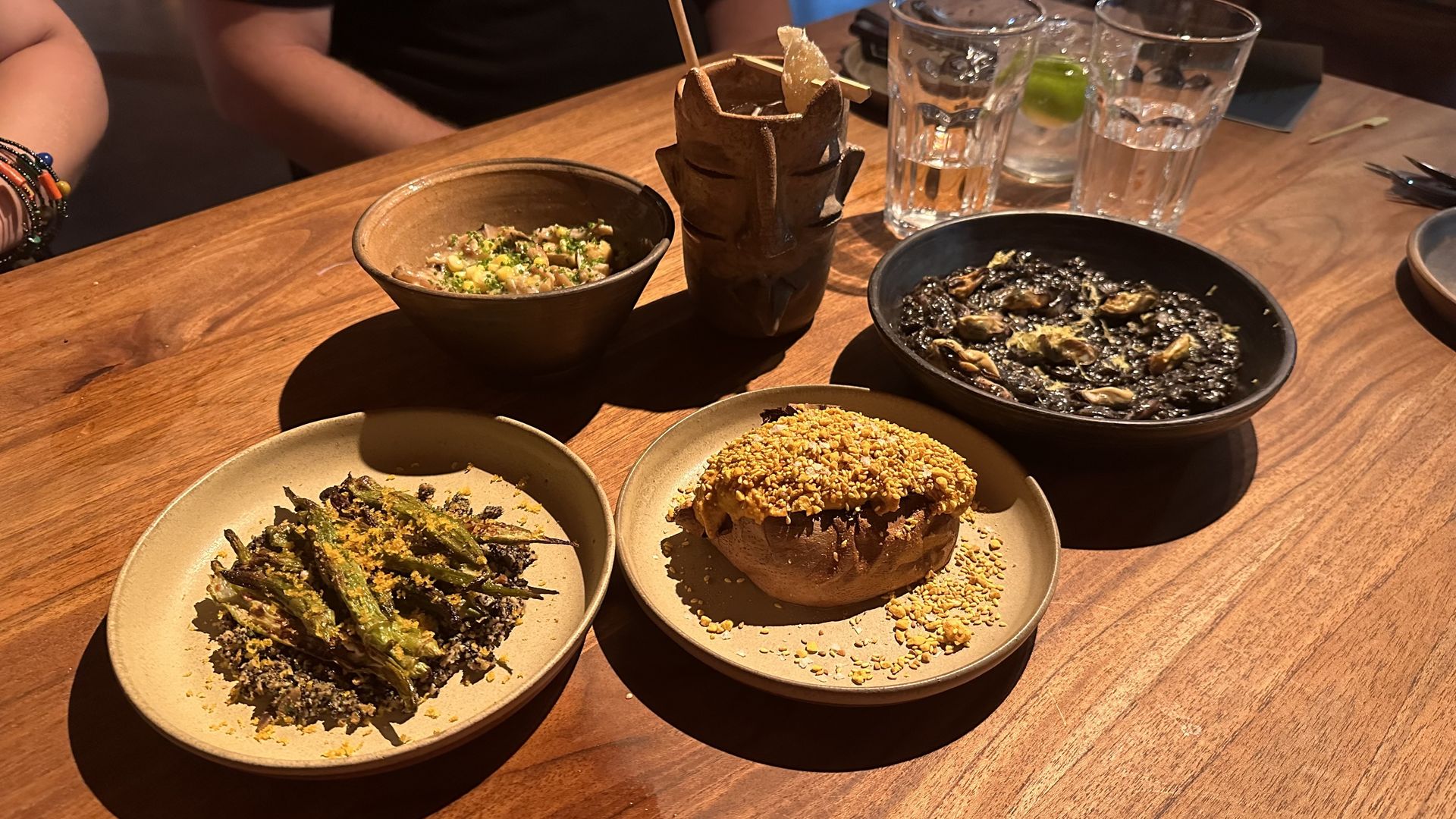 Four plates fill a wooden table. A sculpted cocktail mug sits at the back.