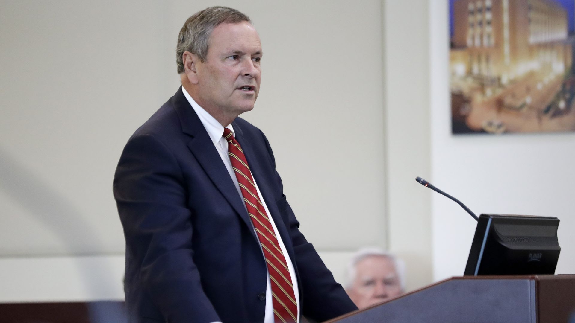 District Attorney Glenn Funk stands at a podium wearing a blue suit and red tie. 