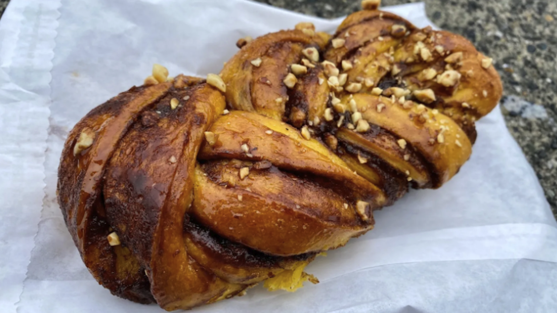 A tubular cinnamon roll with nuts crushed on top.