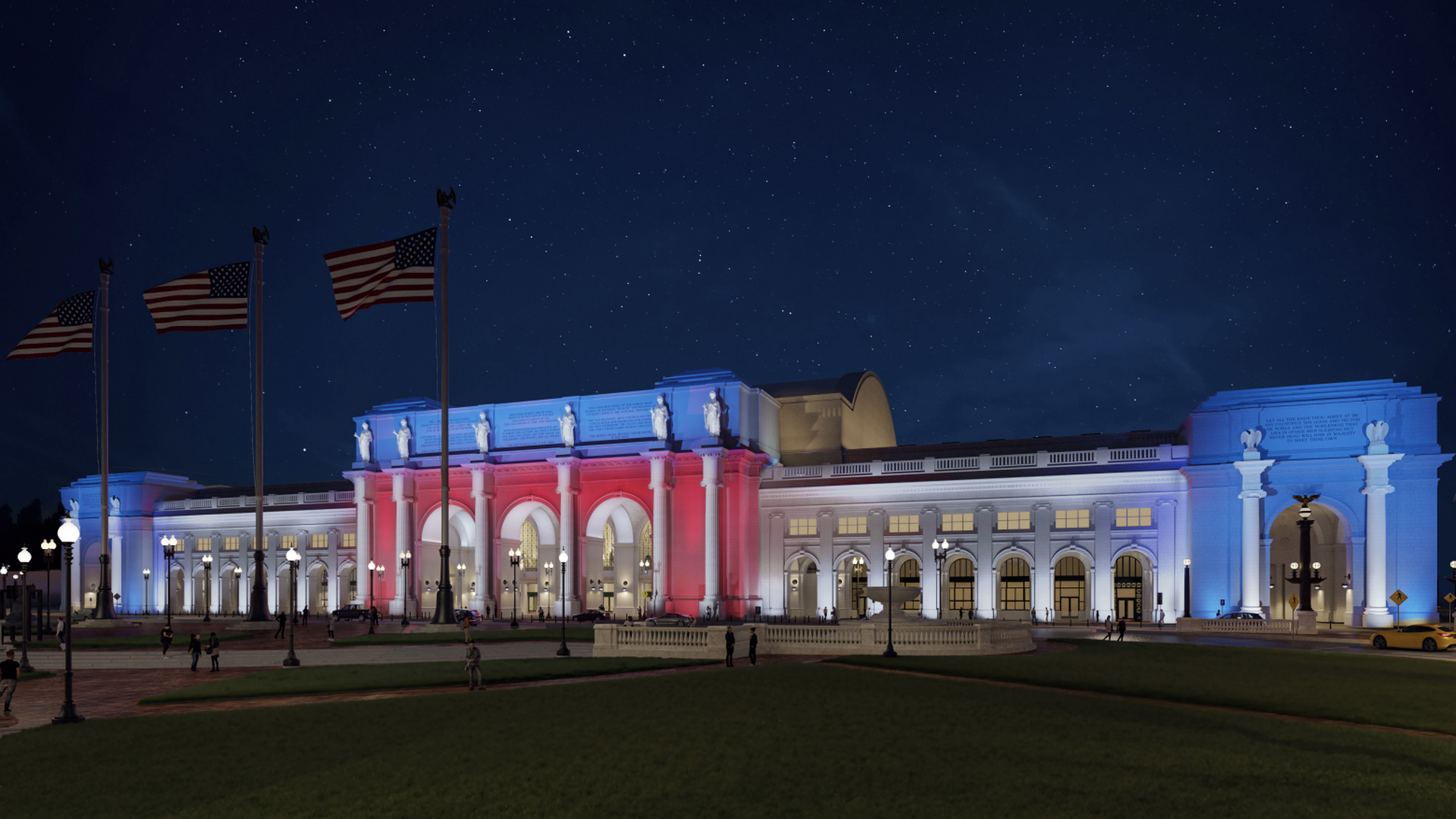 Historic building lit at night with red, white, and blue lights resembling the American flag, with stars visible in the dark sky and several American flags flying on poles nearby.