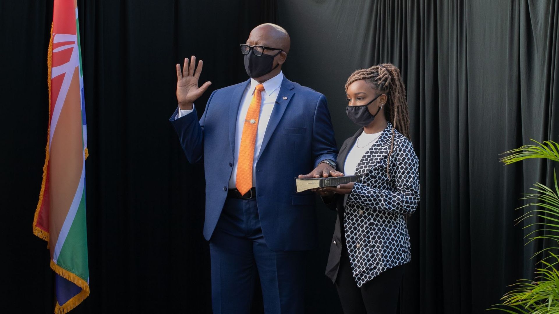 Ken Welch holds his right hand up as he is sworn in, with his daughter next to him holding the Bible. Both wear masks.