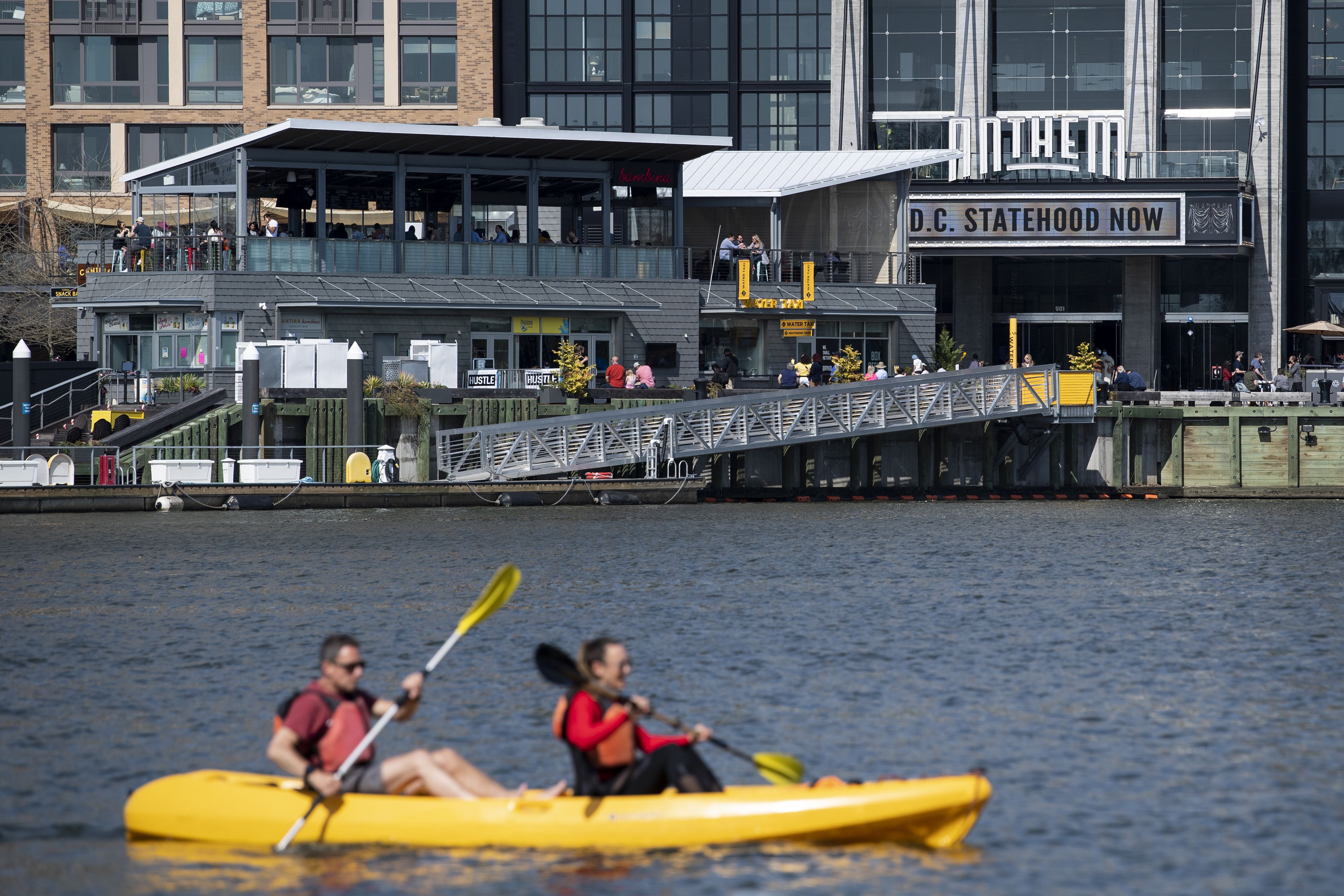 Two people kayak by the Wharf with the Anthem in the background.  
