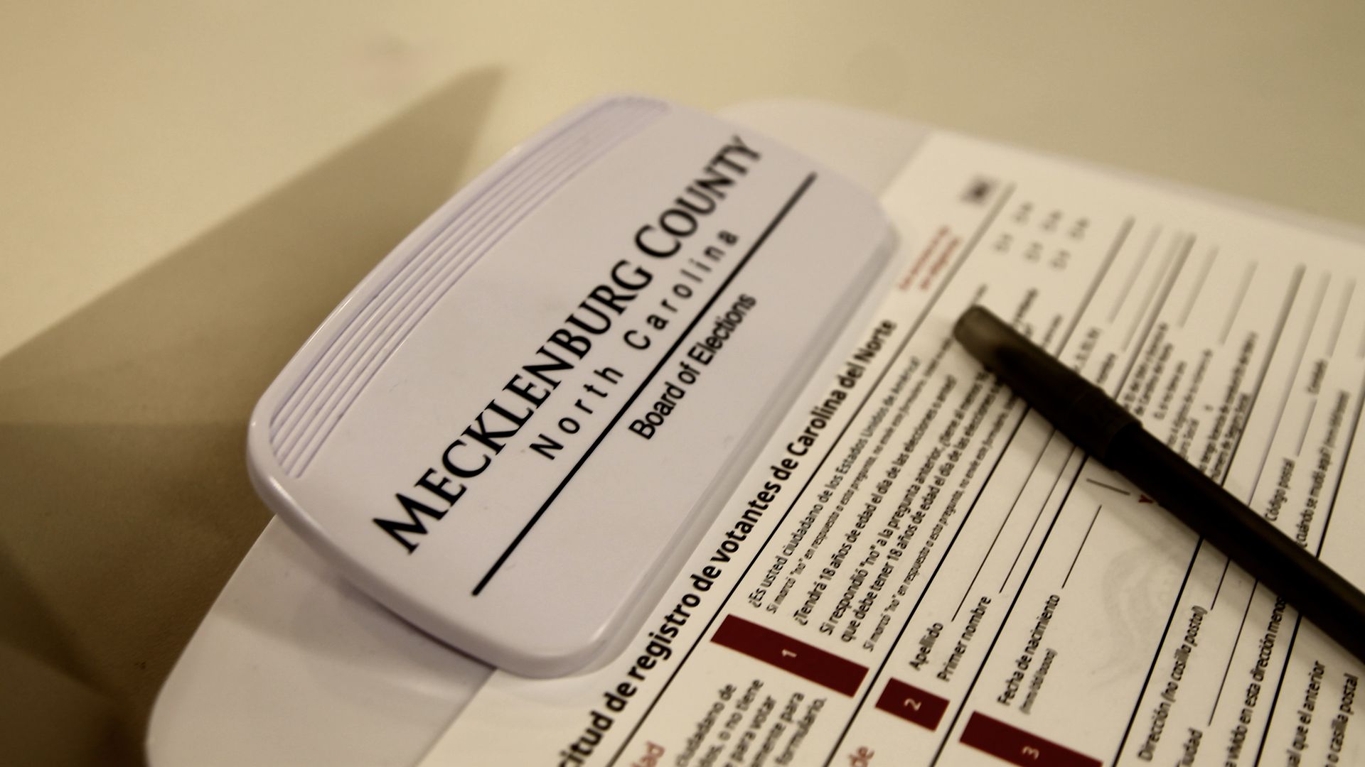 Close-up of a Mecklenburg County, North Carolina Board of Elections document, partly in Spanish, with a black pen resting on it on a light-colored surface.
