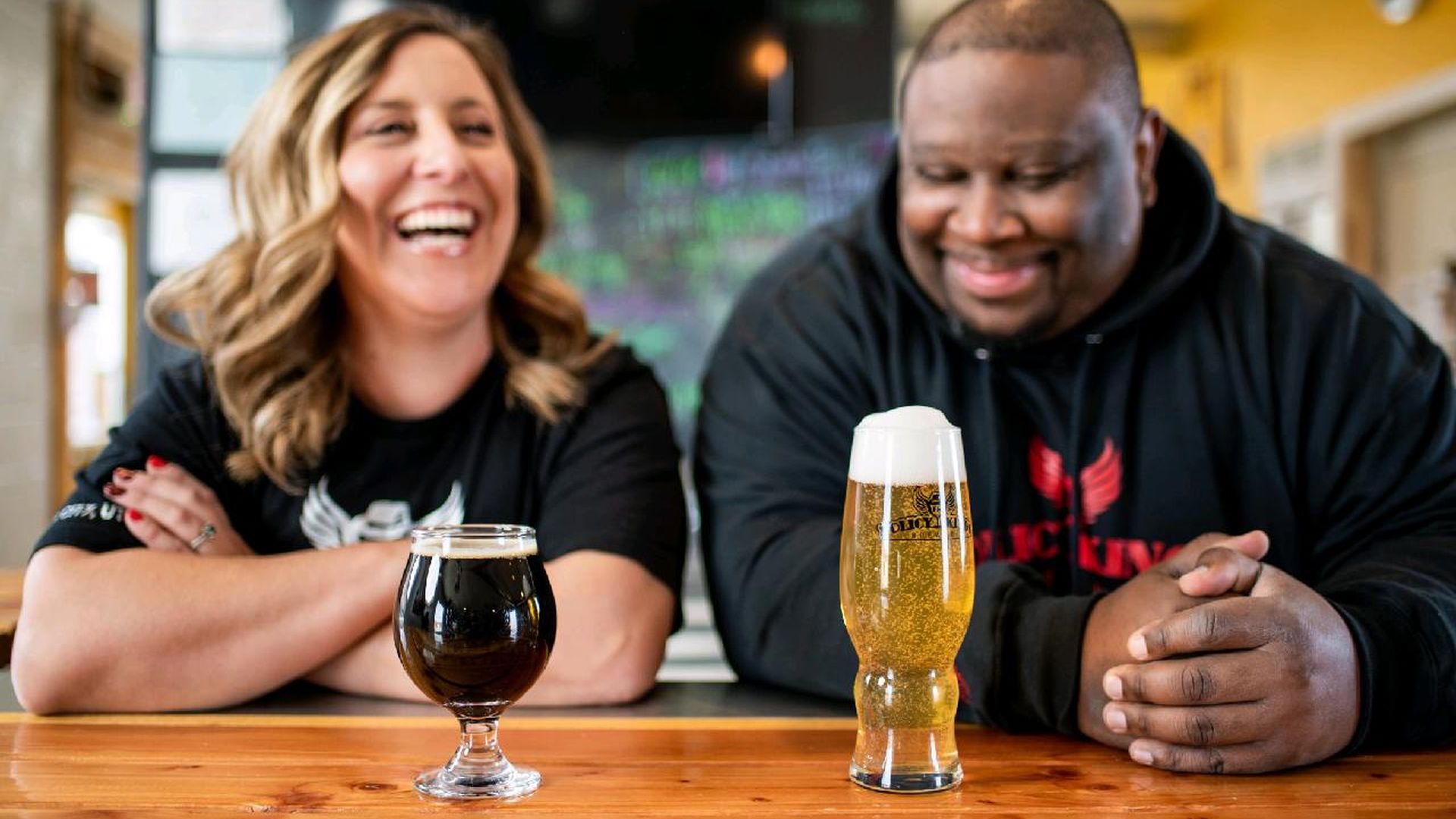 Two people laugh next to glasses of beer.