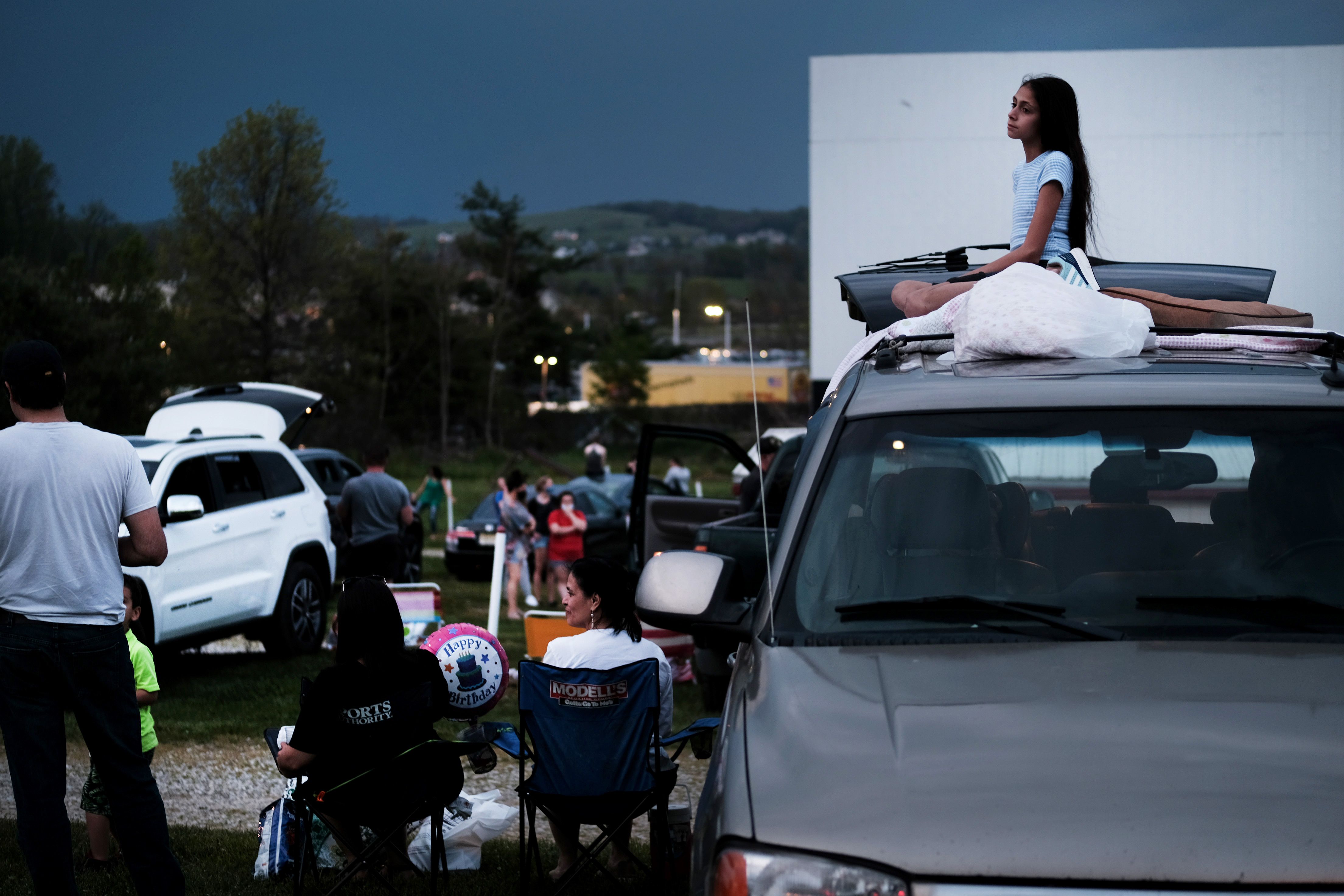 In this image, a girl sits on top of a car 