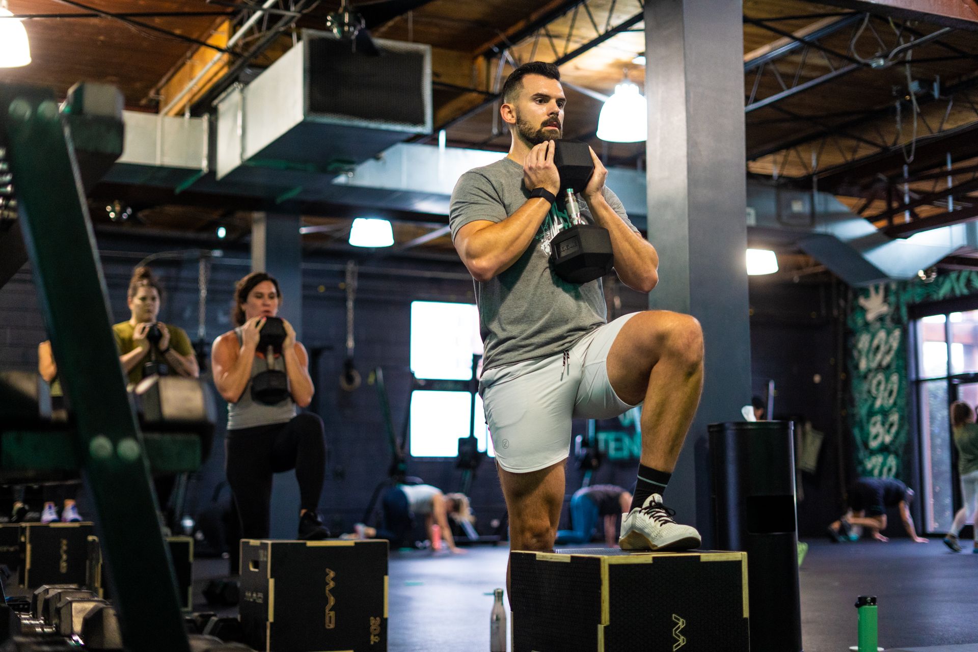A man squatting on a box in a gym.