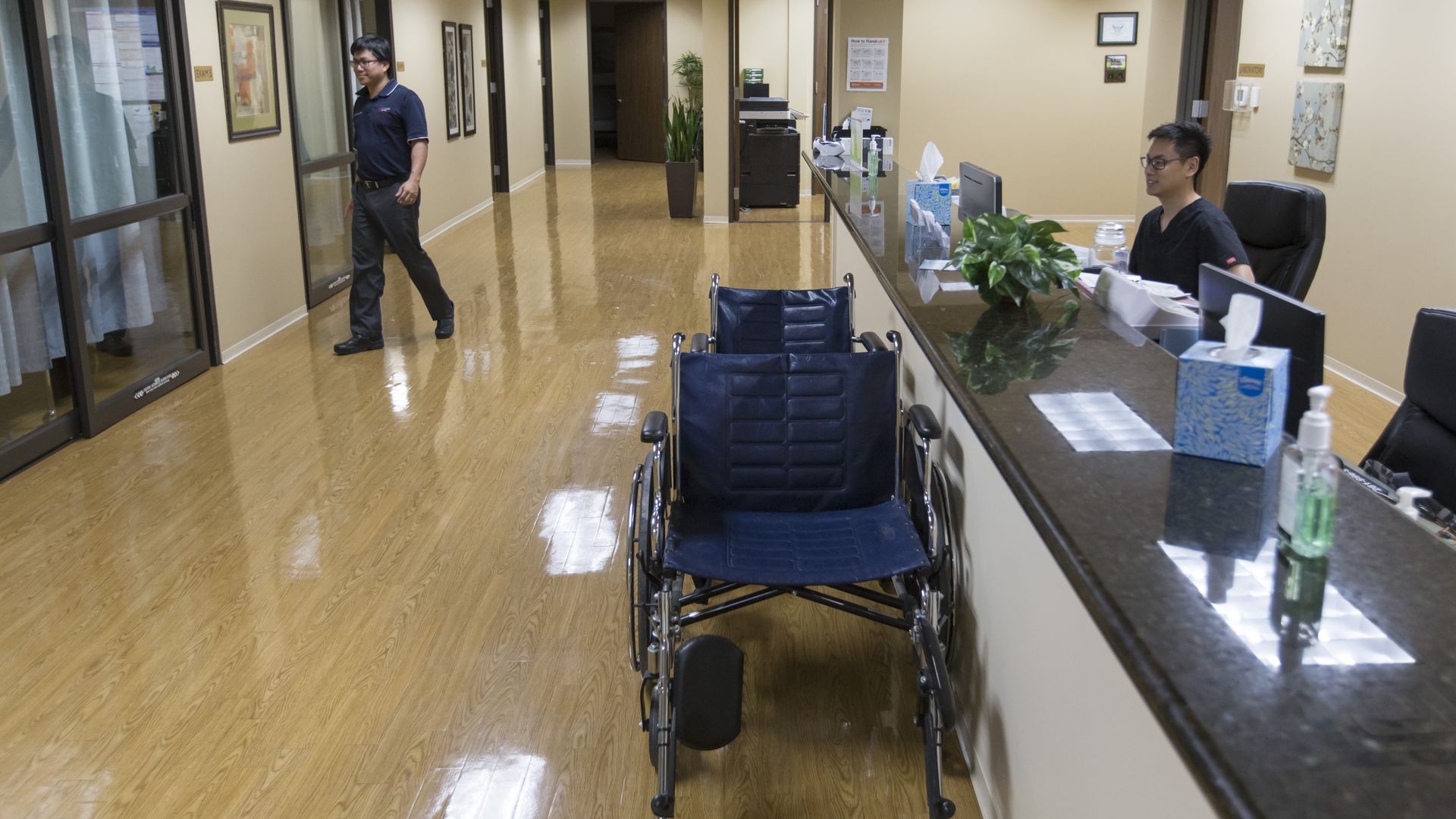 A nurse sits behind a desk in an emergency room with wheelchairs nearby.