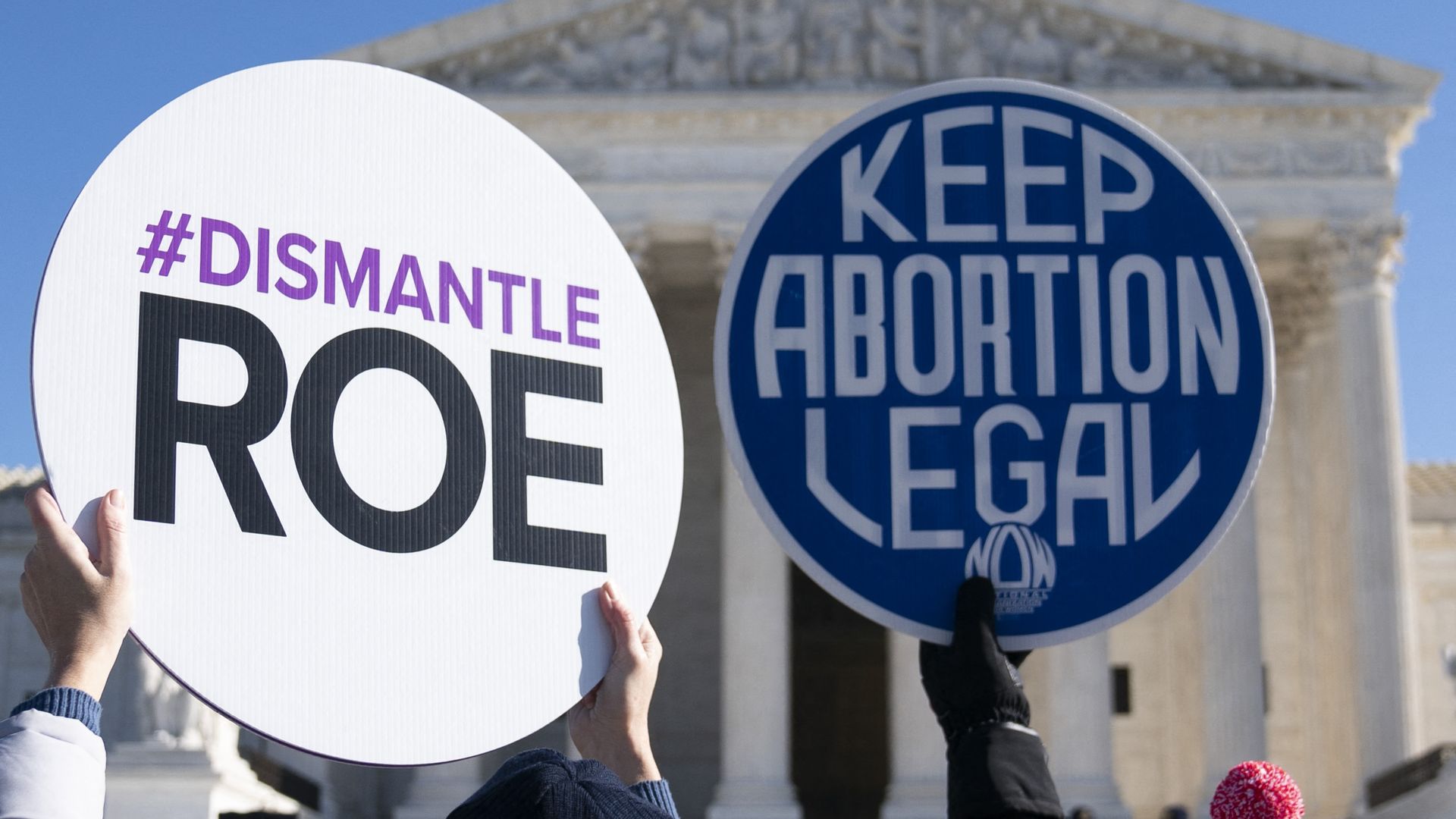 Picture of hands holding signs in front of the Supreme Court, one says "Dismantle Roe" and the other "Keep abortion legal"