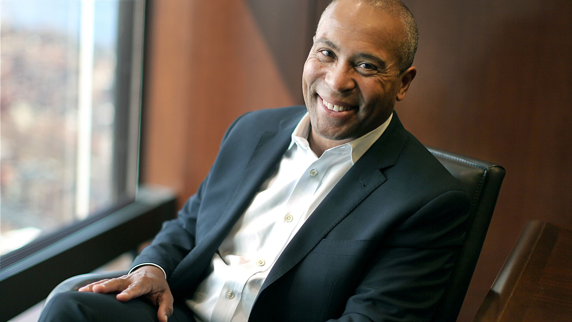 Deval Patrick sits in a chair and smiles at the camera.