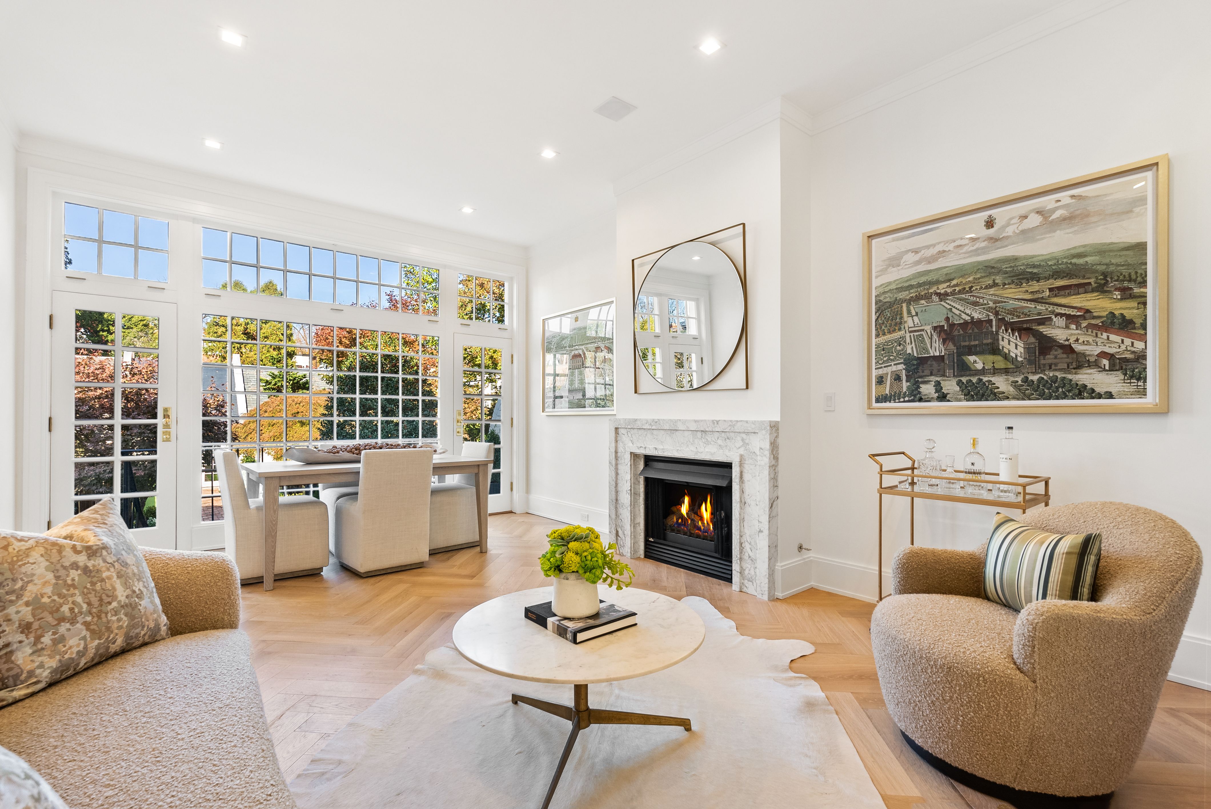 A photo showing a living room with a fireplace and a wall of windows overlooking a garden.