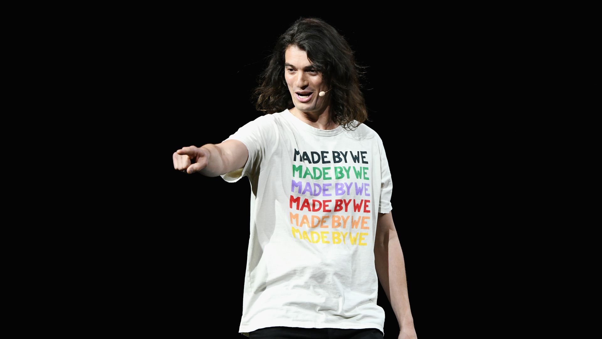 Adam Neumann, in a white t-shirt that says "MADE BY WE," points at an audience member from stage.