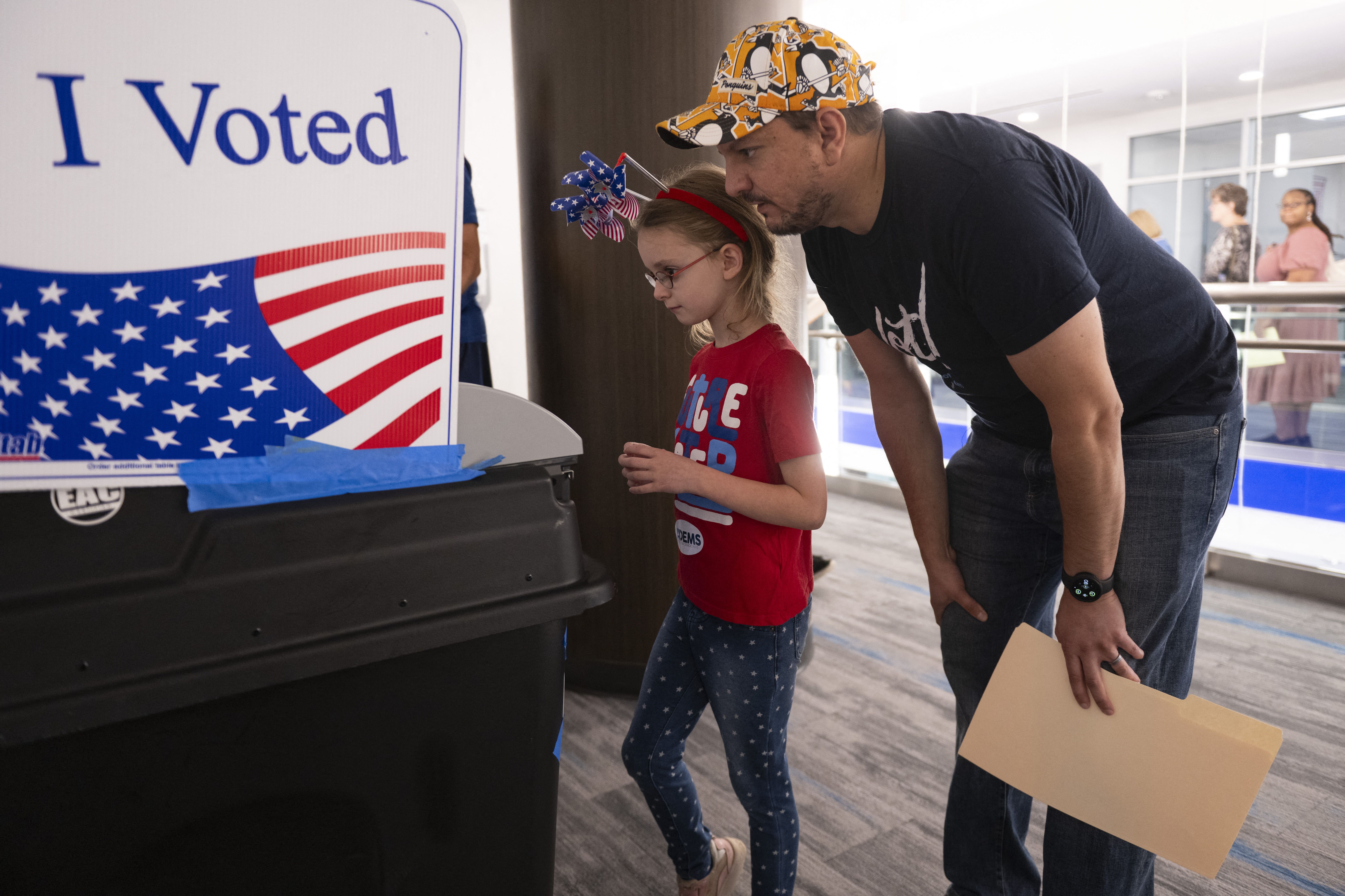 Nick Vucic and his daughter Abigail, 7, watch as a machine records his vote at a polling station in the Elena Bozeman Government Center in Arlington, Virginia, on September 20, 2024. Early in-person voting for the 2024 US presidential election began in Virginia, South Dakota and Minnesota. (Photo by