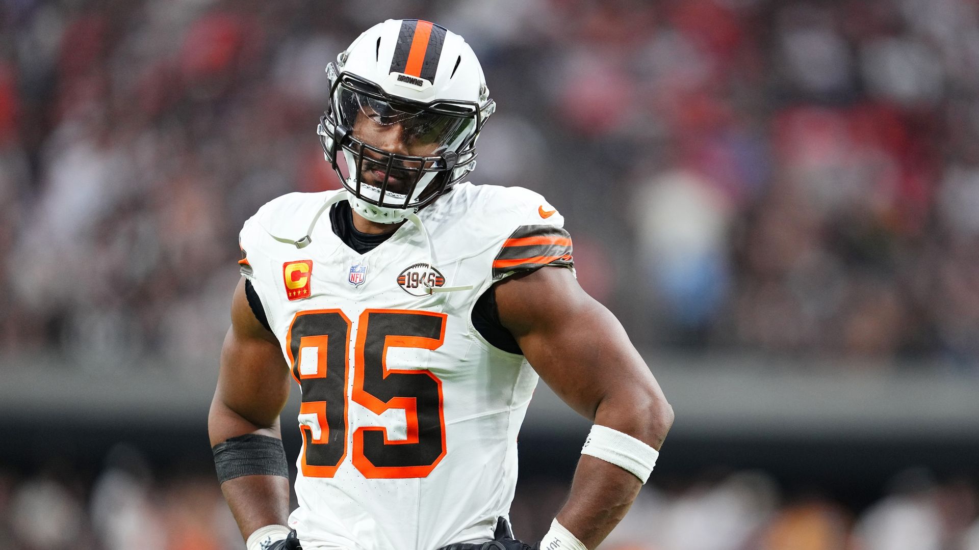 Browns defender Myles Garrett stands on the field with all-white uniform on and hands on hip. 