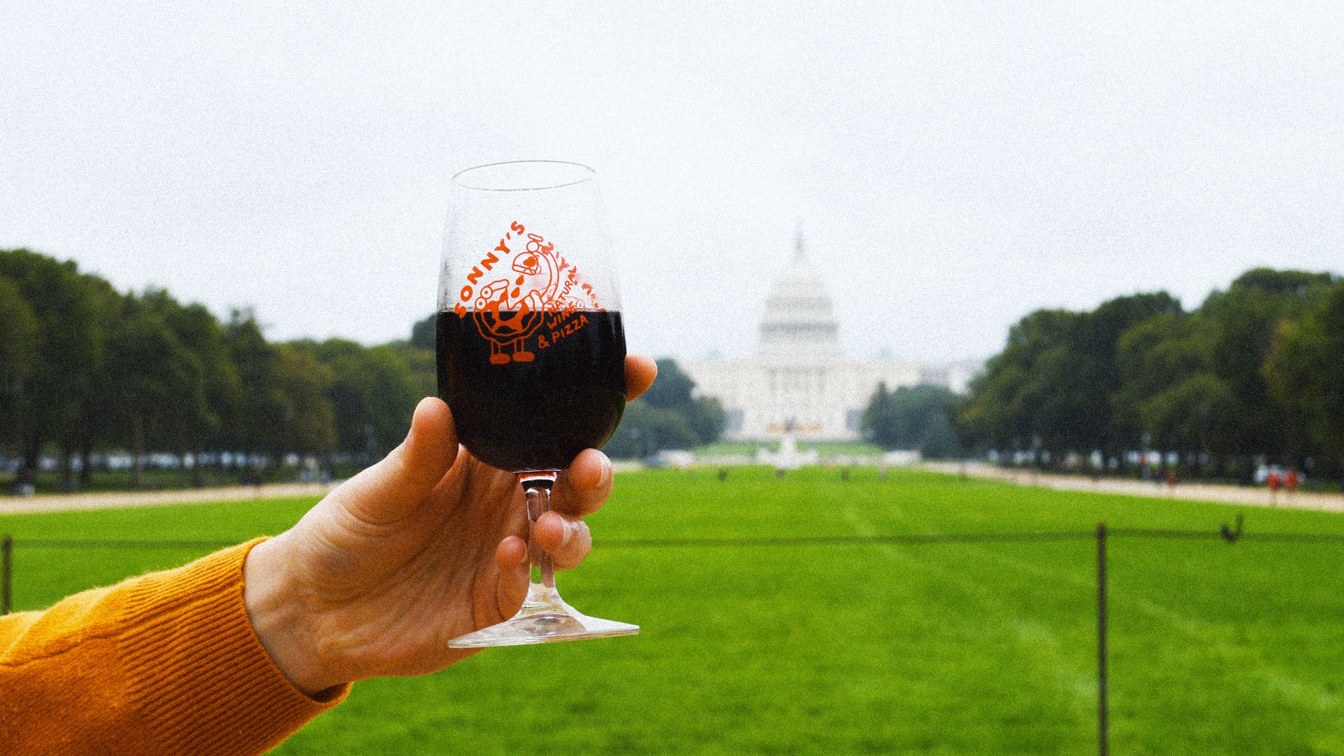 An arm holding a glass of red wine in front of the US Capitol