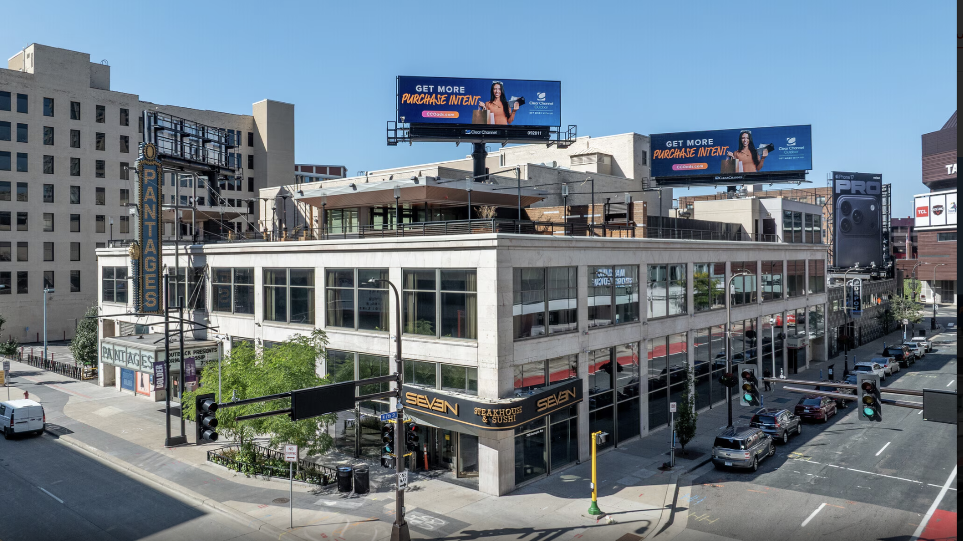 City street intersection with a modern two-story building housing Seven Steakhouse & Sushi, featuring large windows and a rooftop bar under a clear blue sky.