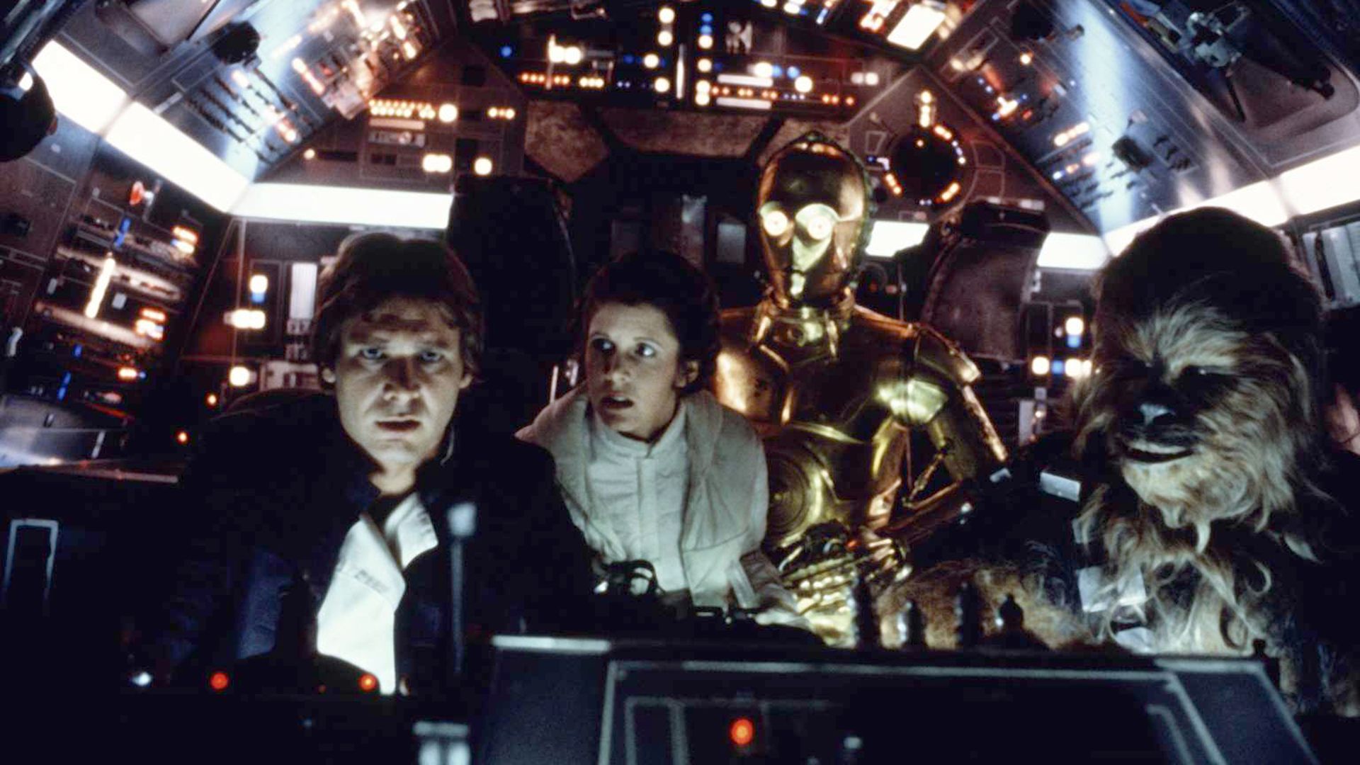 Inside a spaceship cockpit with colorful controls, four characters including a man, a woman in white, a gold robot, and a furry creature are closely observing the controls.