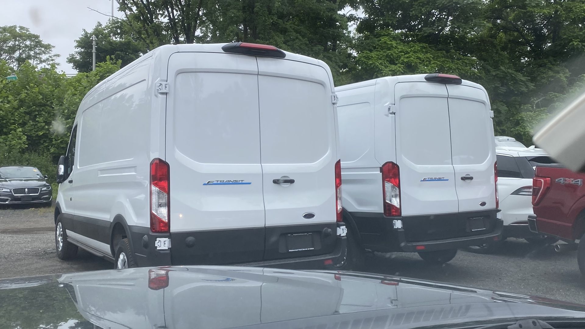 A photo of two Ford E-Transit electric vans, parked in a dealer's lot.