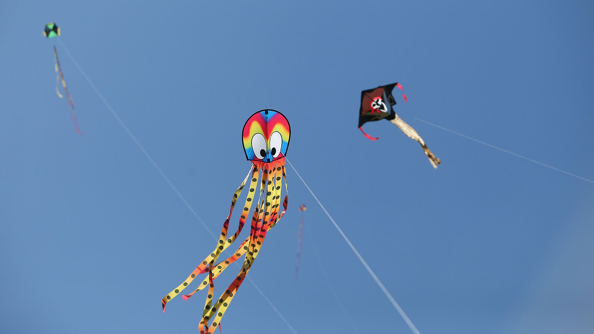 A kite that looks like an rainbow-colored octopus flies in a clear blue sky