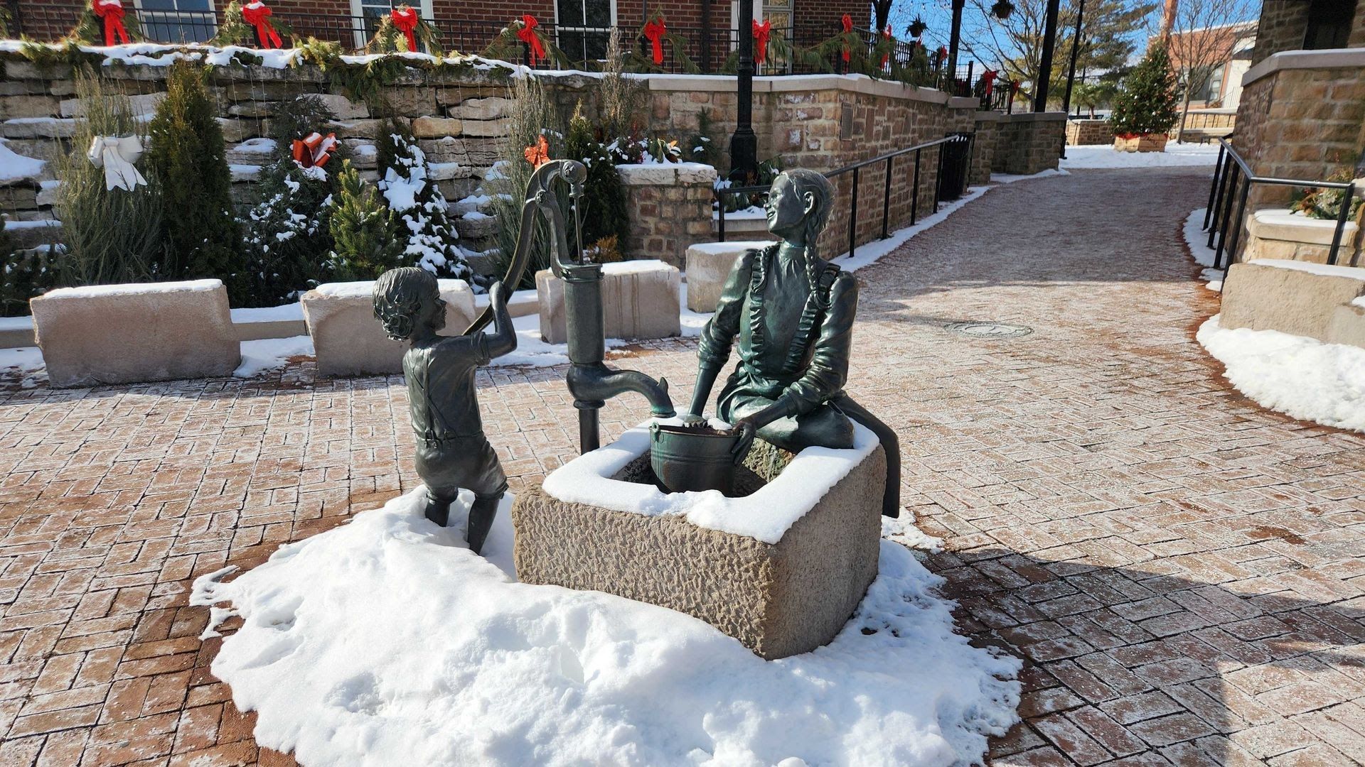 A snow-covered sculpture of two kids working an old-fashioned town water pump.