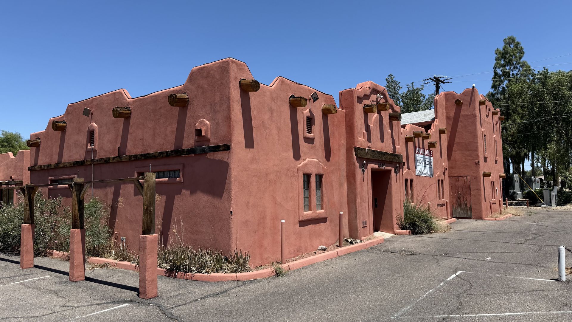 A one-story, adobe-style building with irregularly shaped edge along the roof and logs sticking out at intervals near the top in the style of support beams.