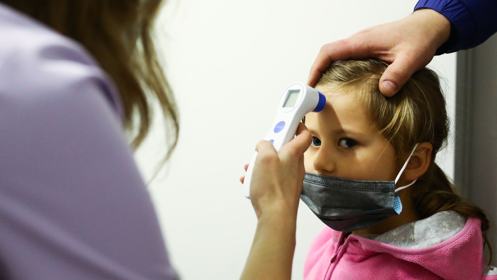 A photo of a child getting her temperature taken.