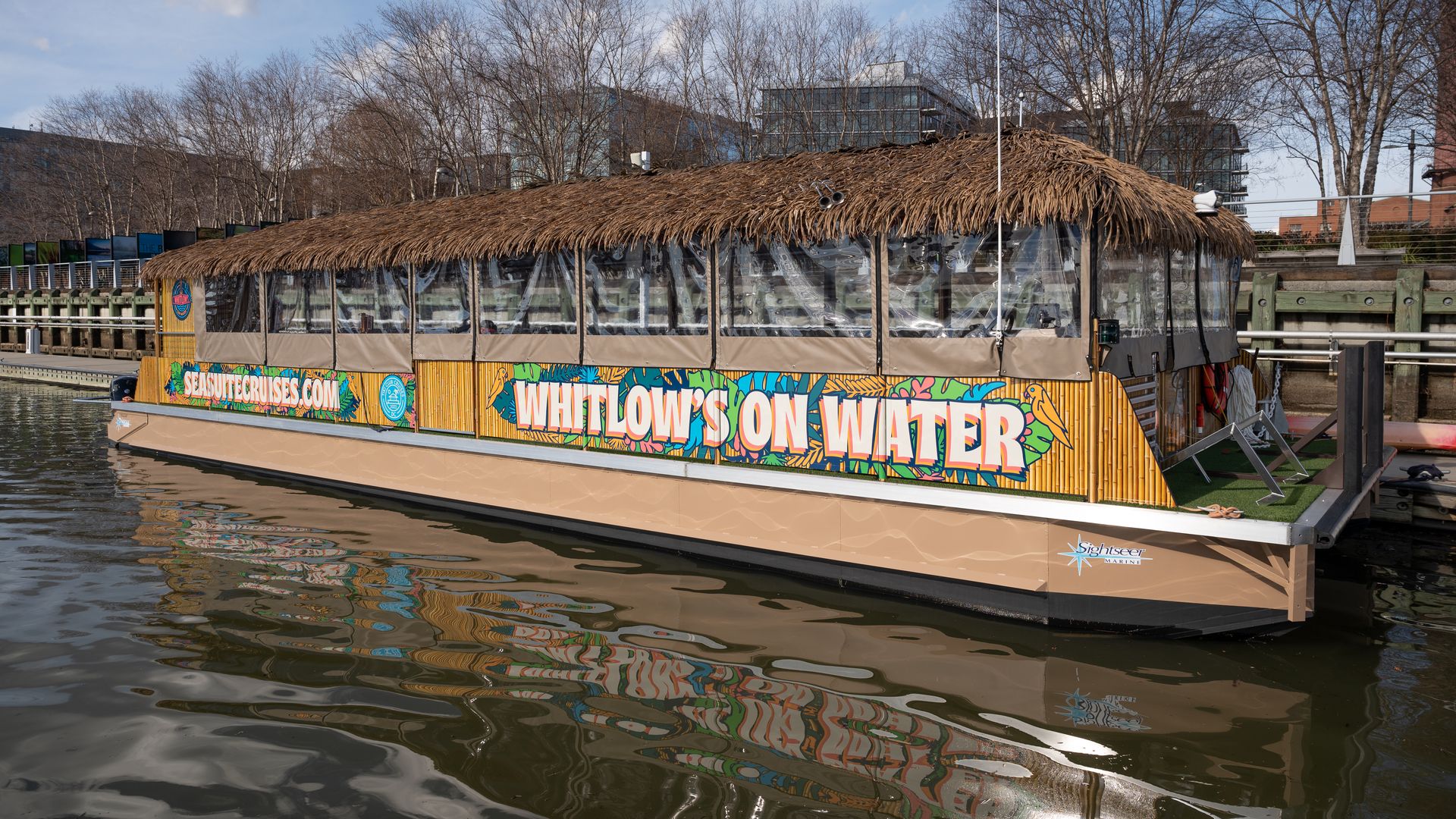 A tiki boat covered in brown thatched roof with a colorful "Whitlow's on the Water" decal