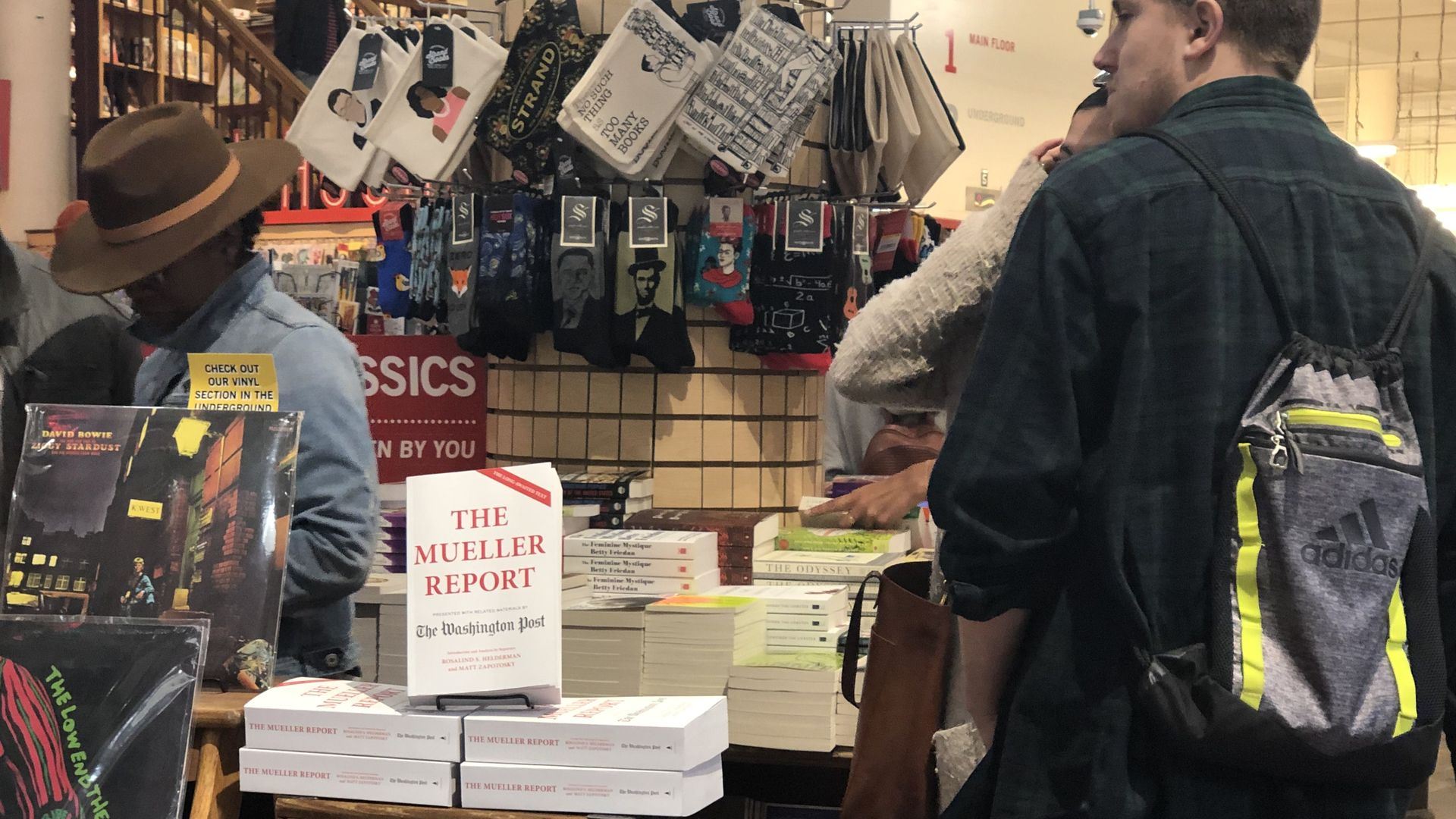 In this image, book shoppers stand around a display table with a stack of Mueller report books.