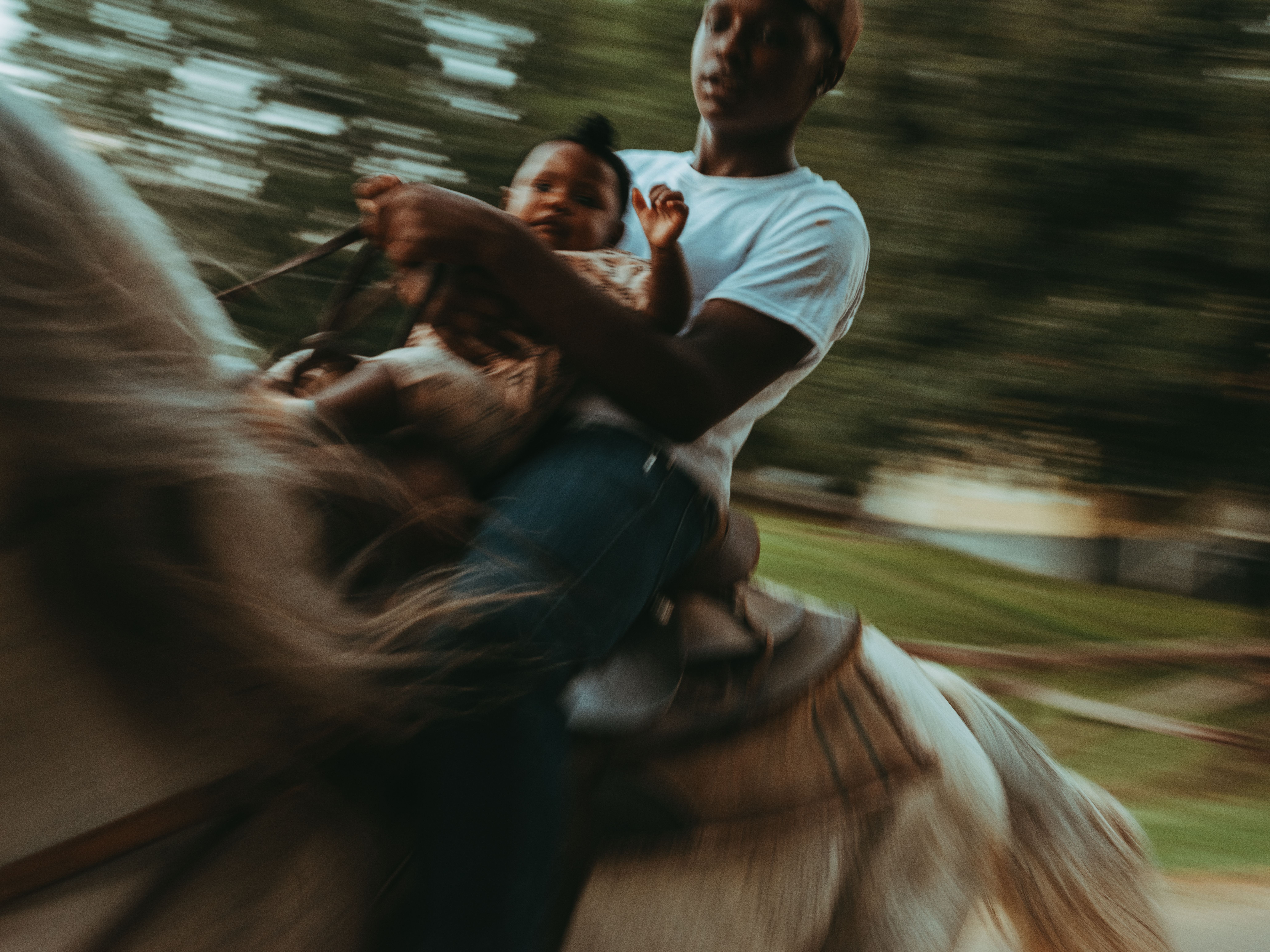 A Black parent rides a horse with a small child.