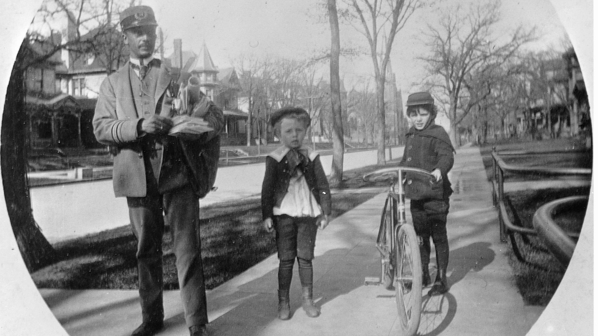 A kid holding a bicycle, next to another kid and a mail carrier