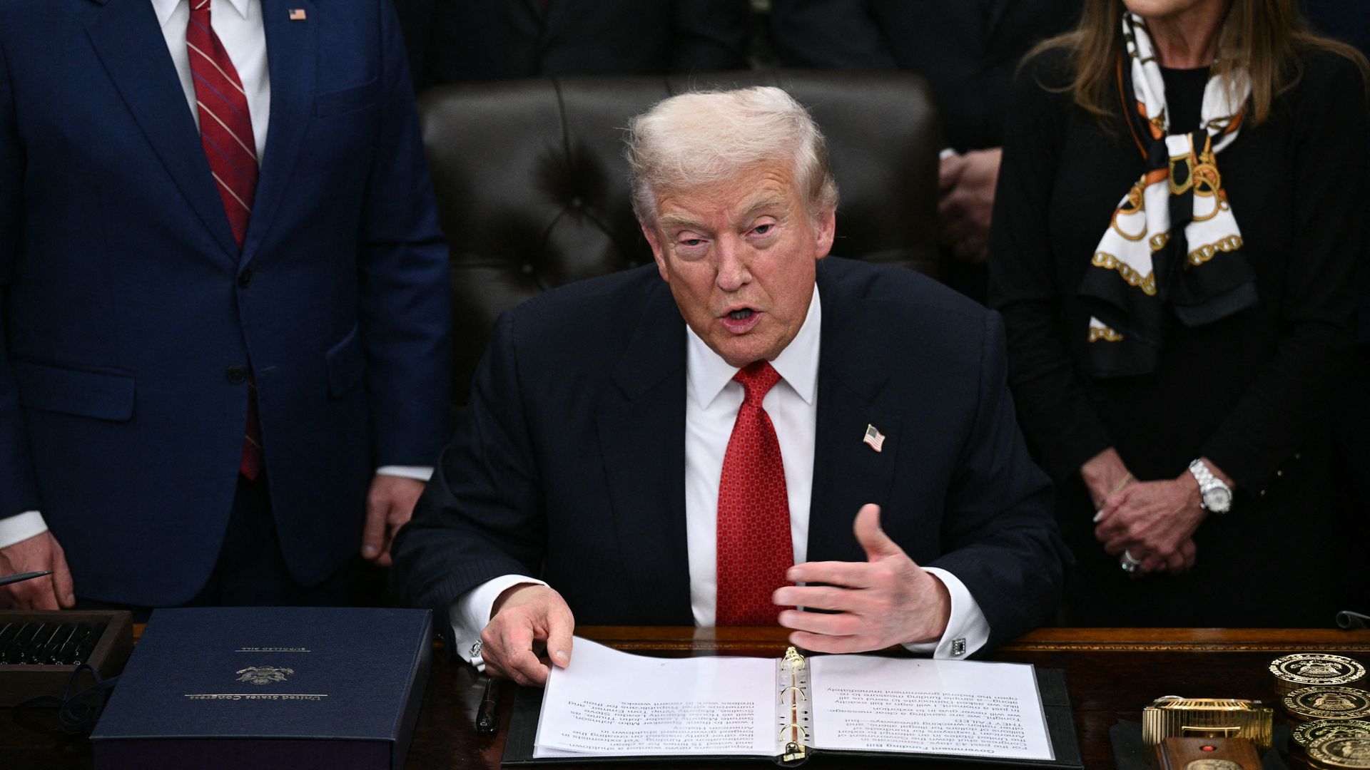 President Trump, in a dark suit and red tie, seated in the Oval Office. 