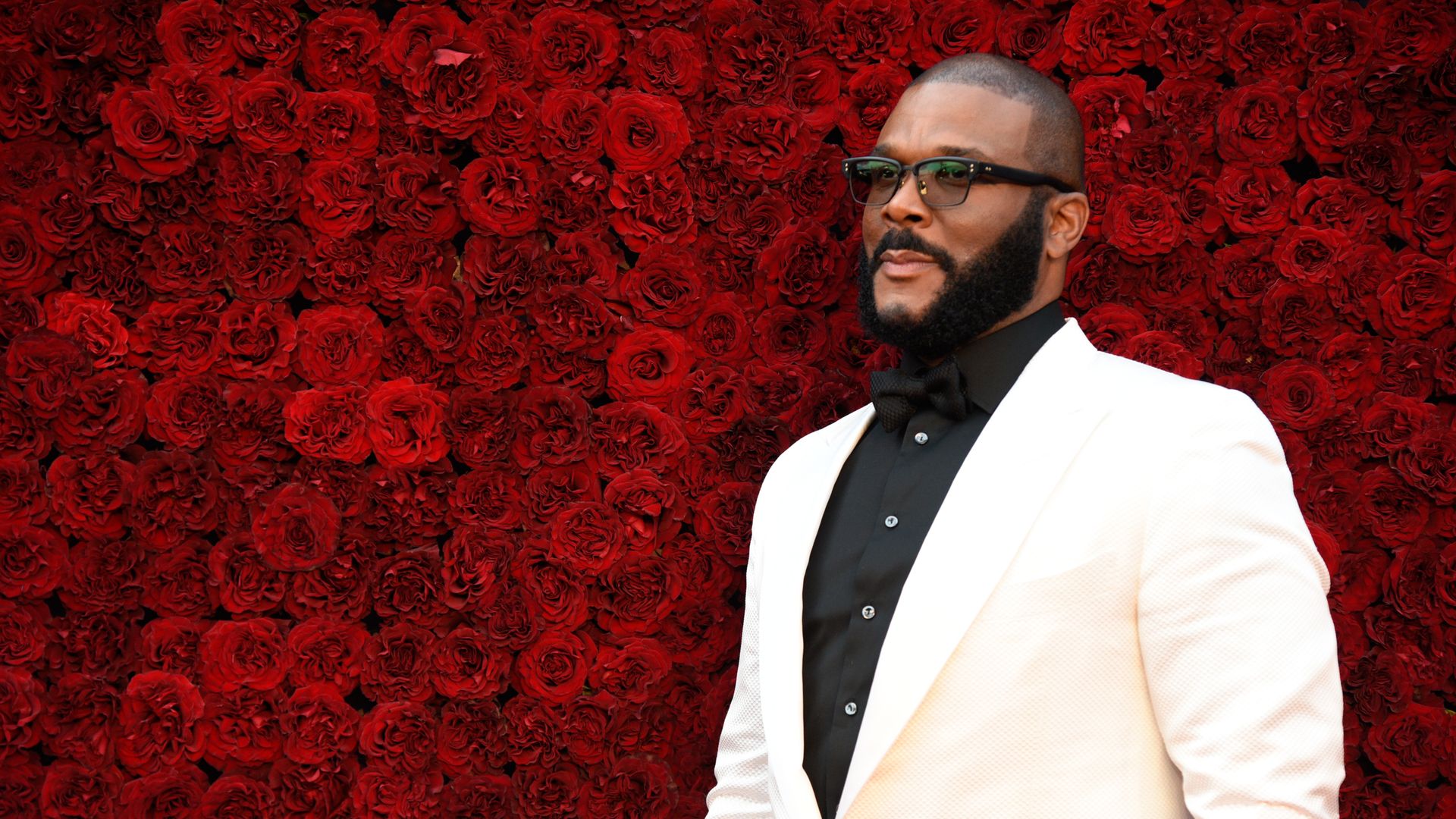 Tyler Perry standing in front of a decorative wall of roses.