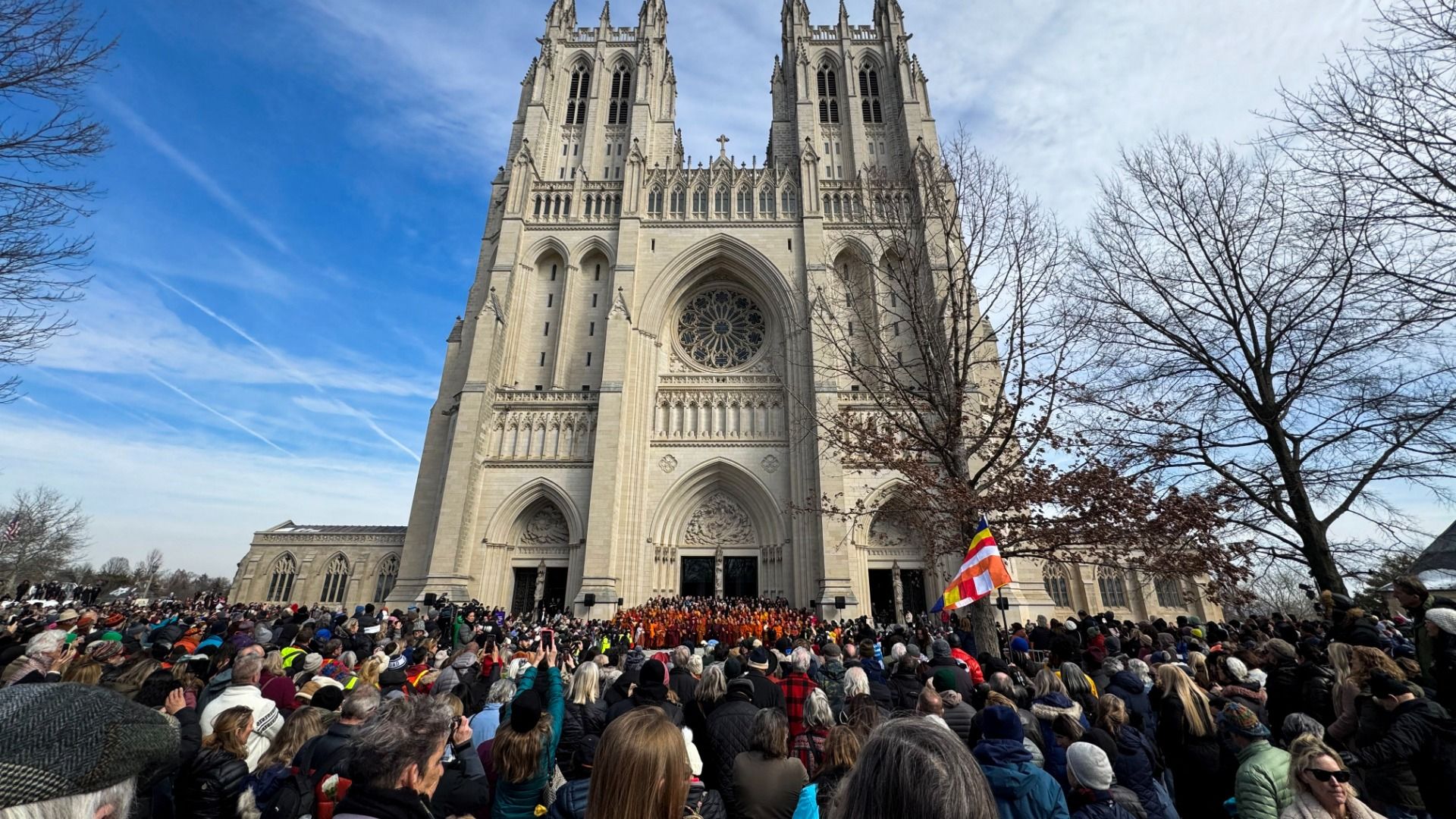 A crowd is gathered in front of a group of Buddhist monks standing on the steps of the Washington National Cathedral. 
