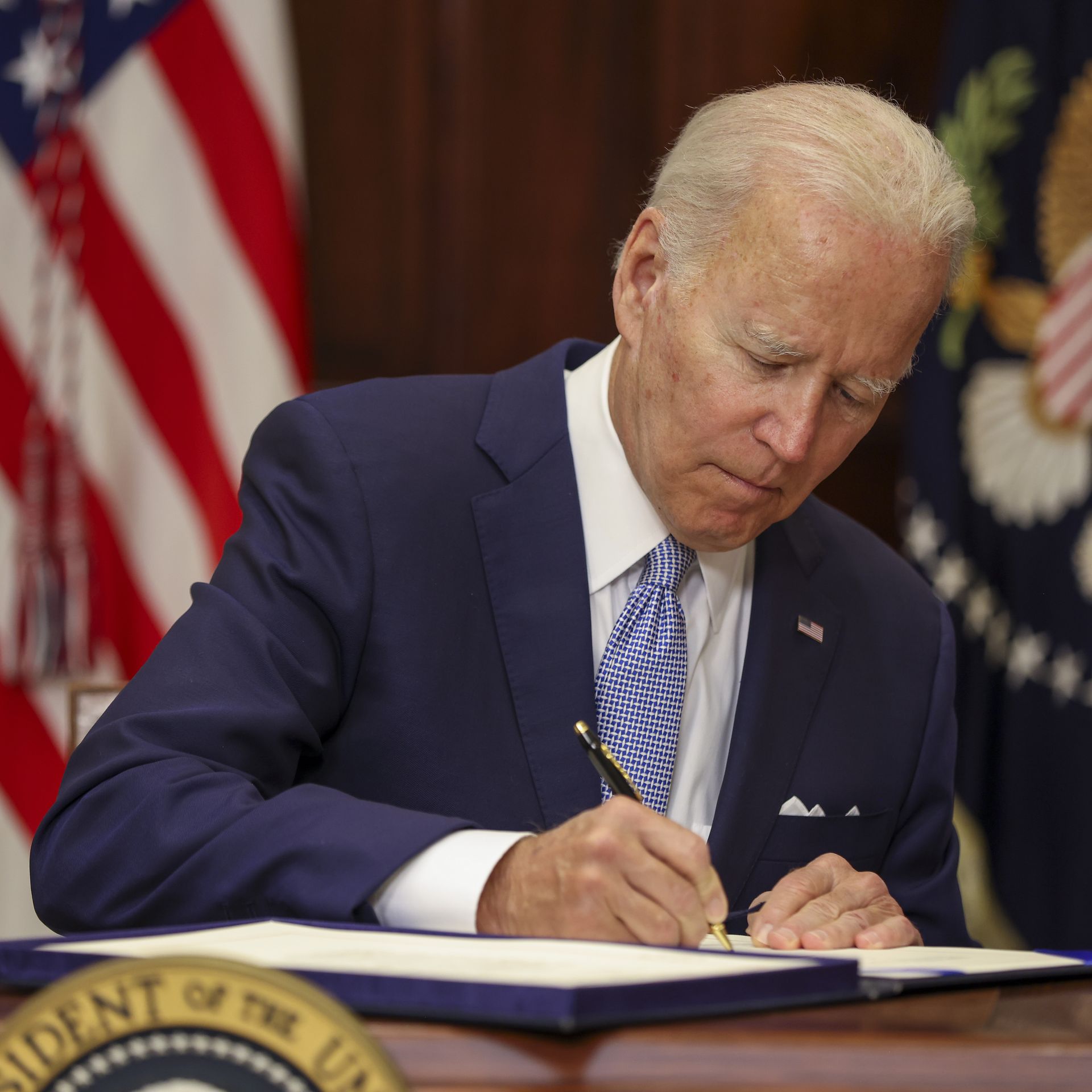 President Biden signing some papers in front of a flag
