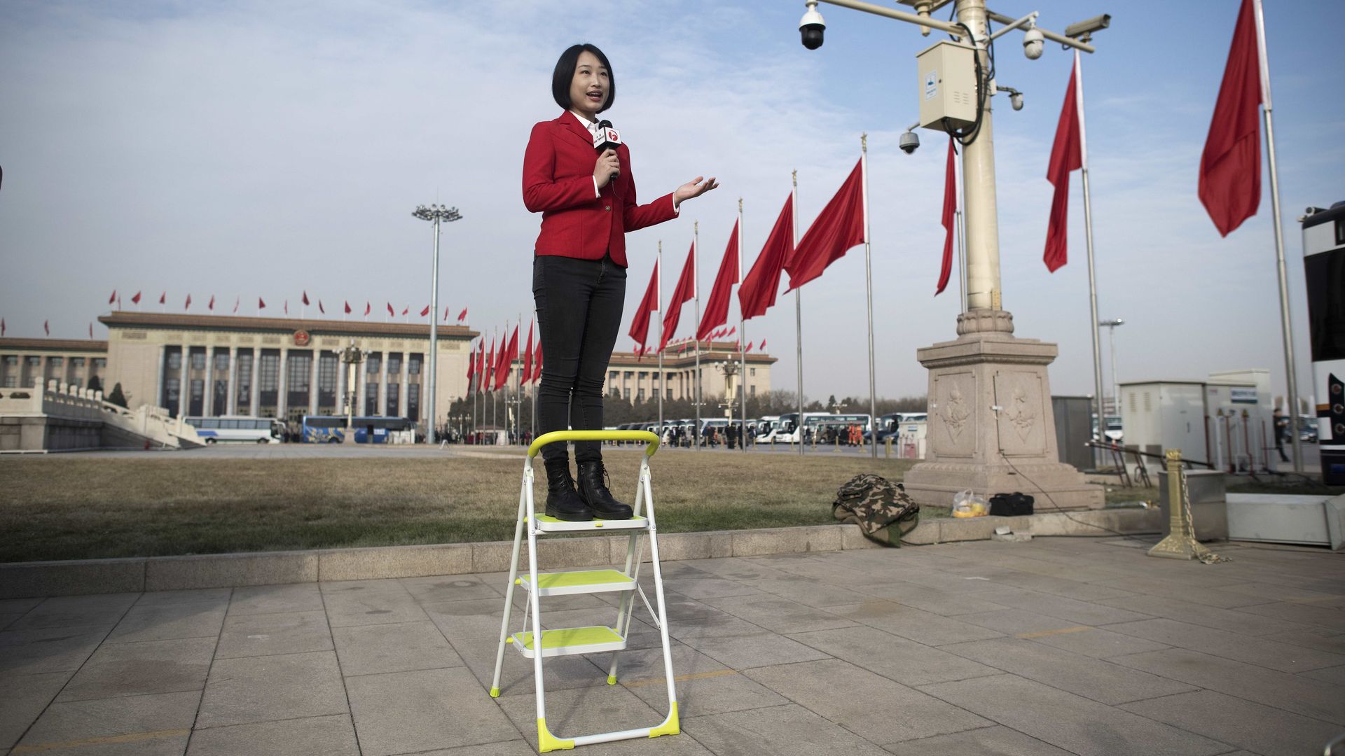 Chinese female journalist standing on step-ladder giving a television presentation