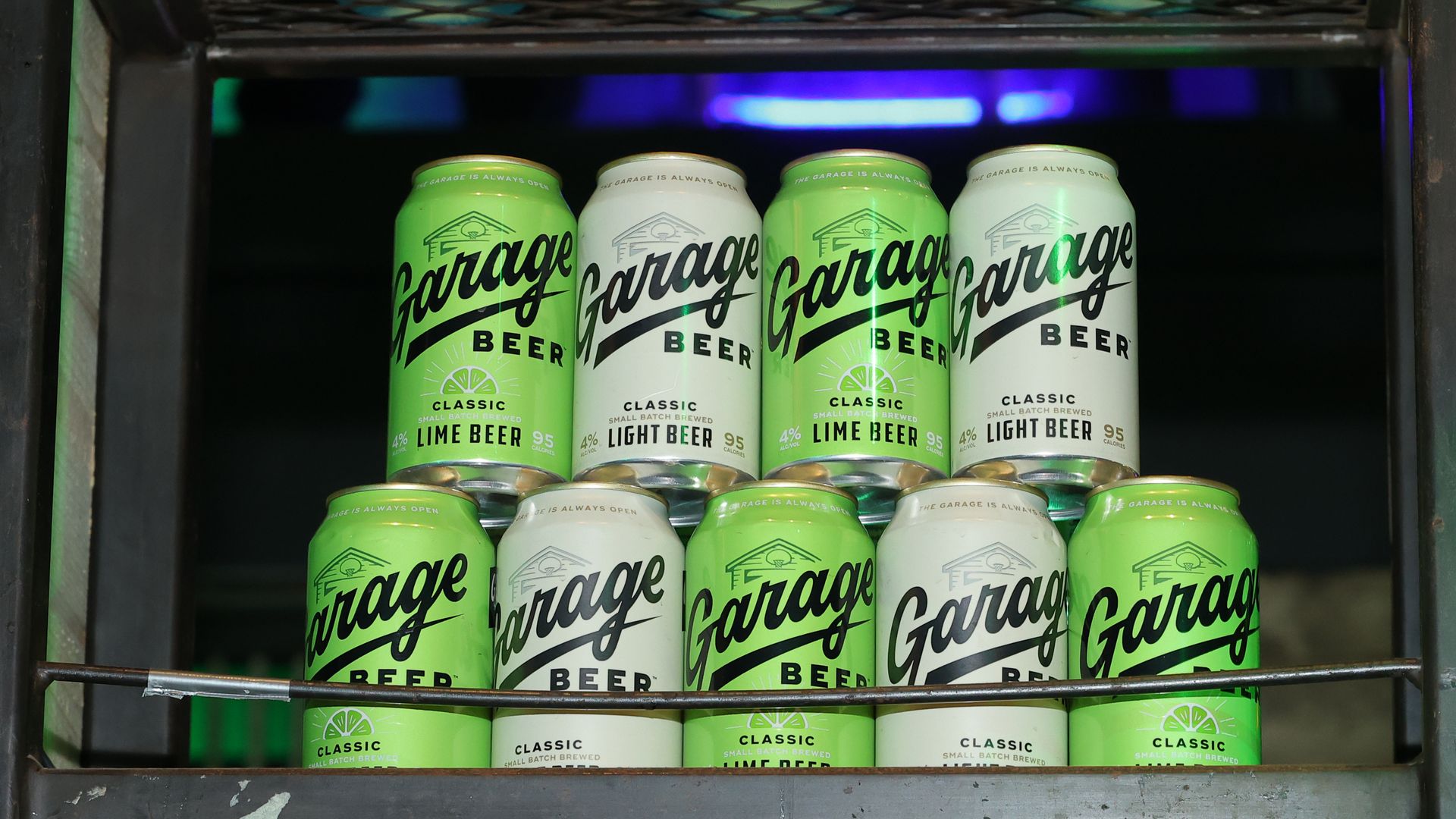Several lime-green and white Garage Beer cans stacked on a metal shelf inside a dark display, with labels reading Classic Lime Beer and Classic Light Beer.