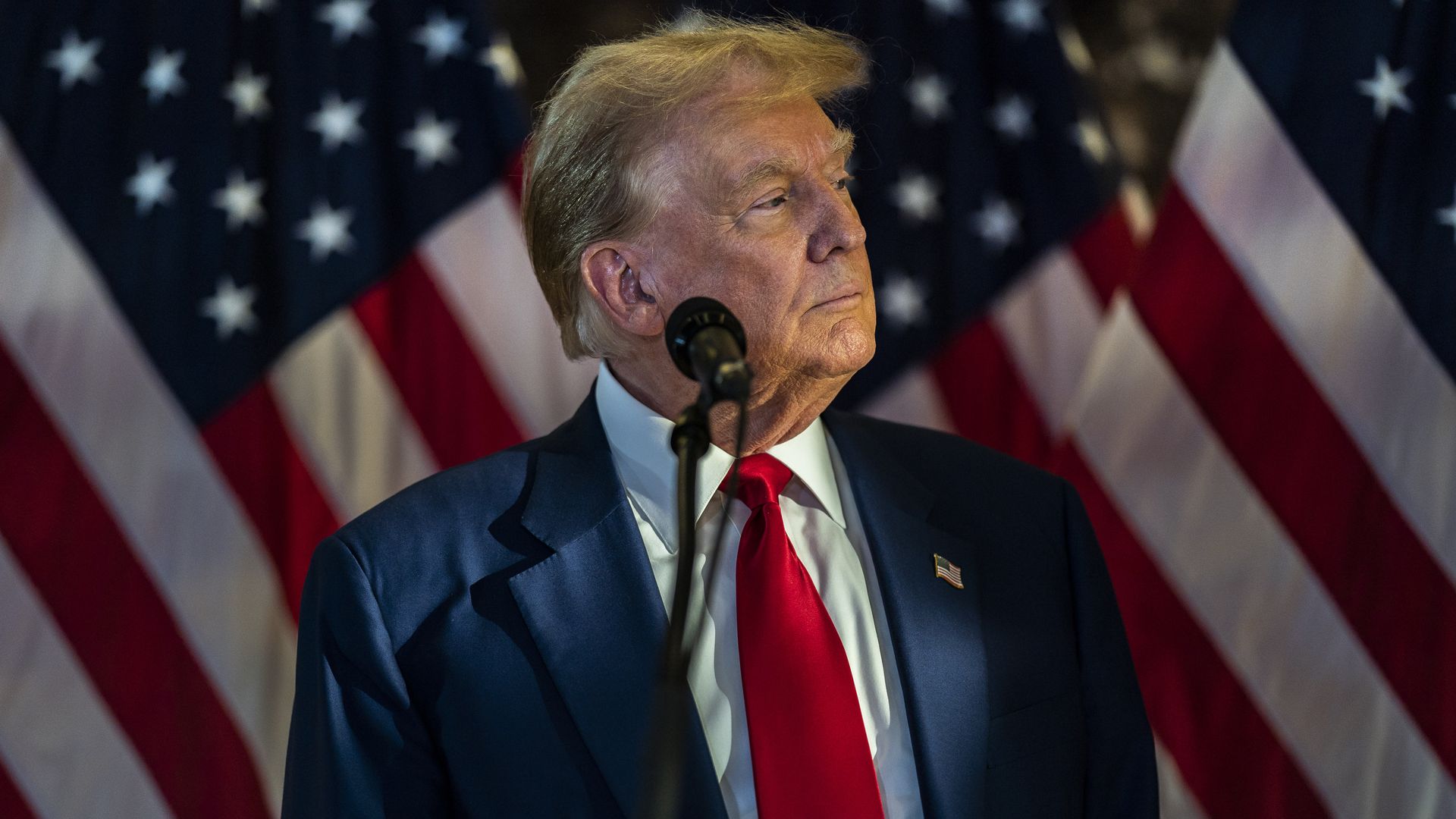 Trump stands in front of a microphone against a US flag backdrop