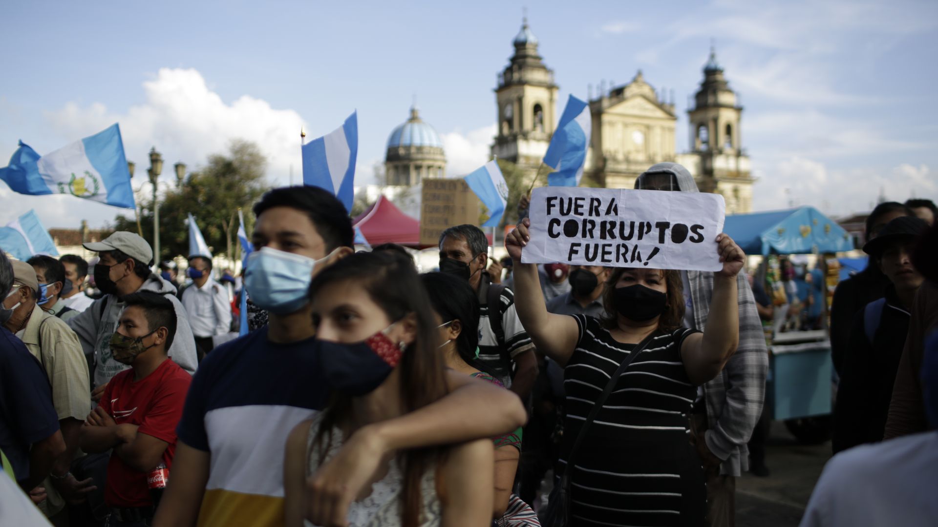 A couple at a protest stands in front of a sign in Spanish in front of a colonial church in Guatemala City.