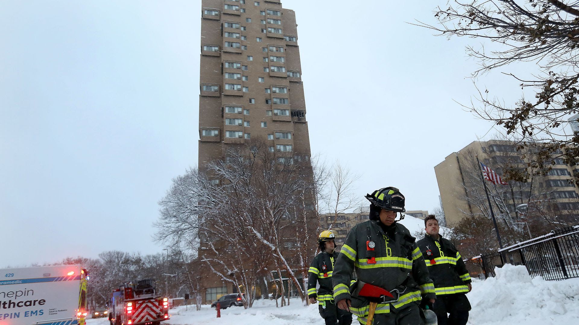 Three Minneapolis firefighters leave a high-rise building fire with their heads down on a snowy winter day.