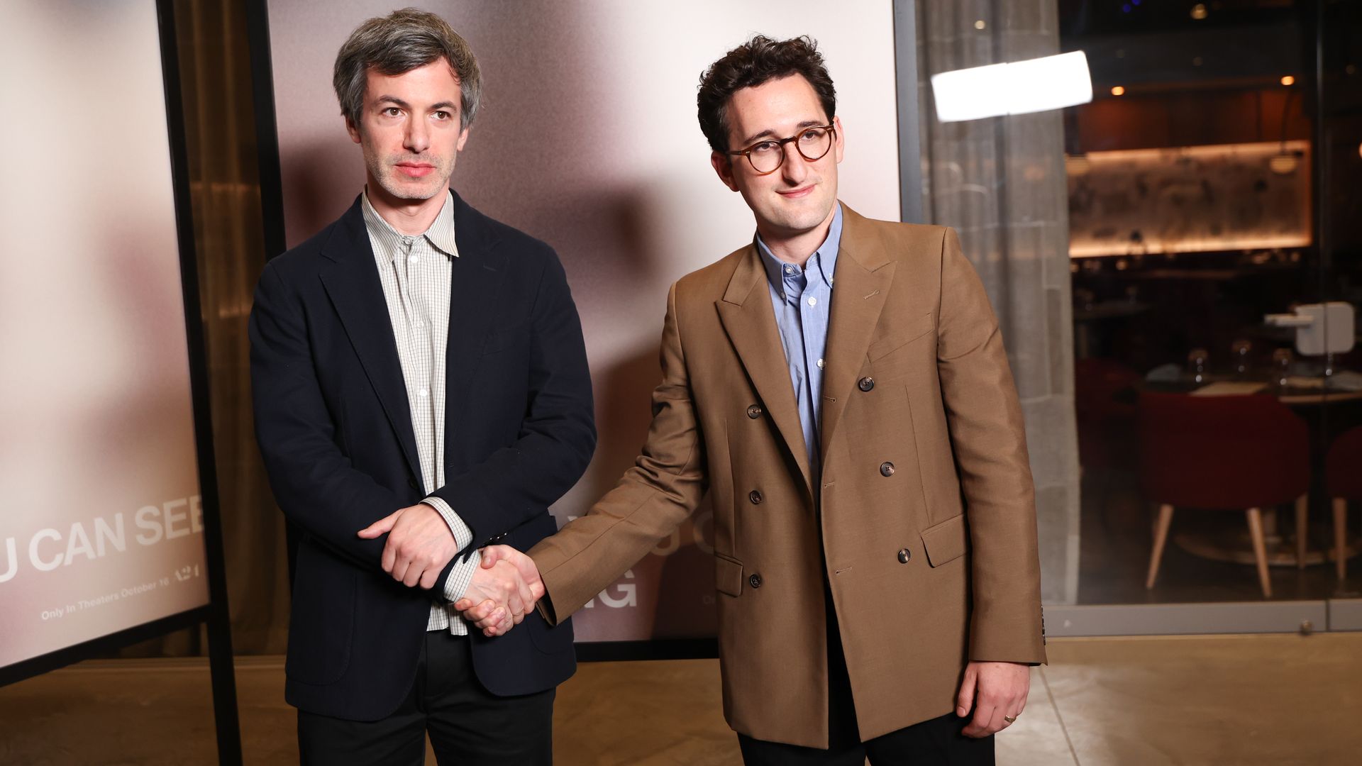 Nathan Fielder(left) and Lance Oppenheim attend "You Can See Everything" Photocall. They are shaking hands and looking at the camera. 